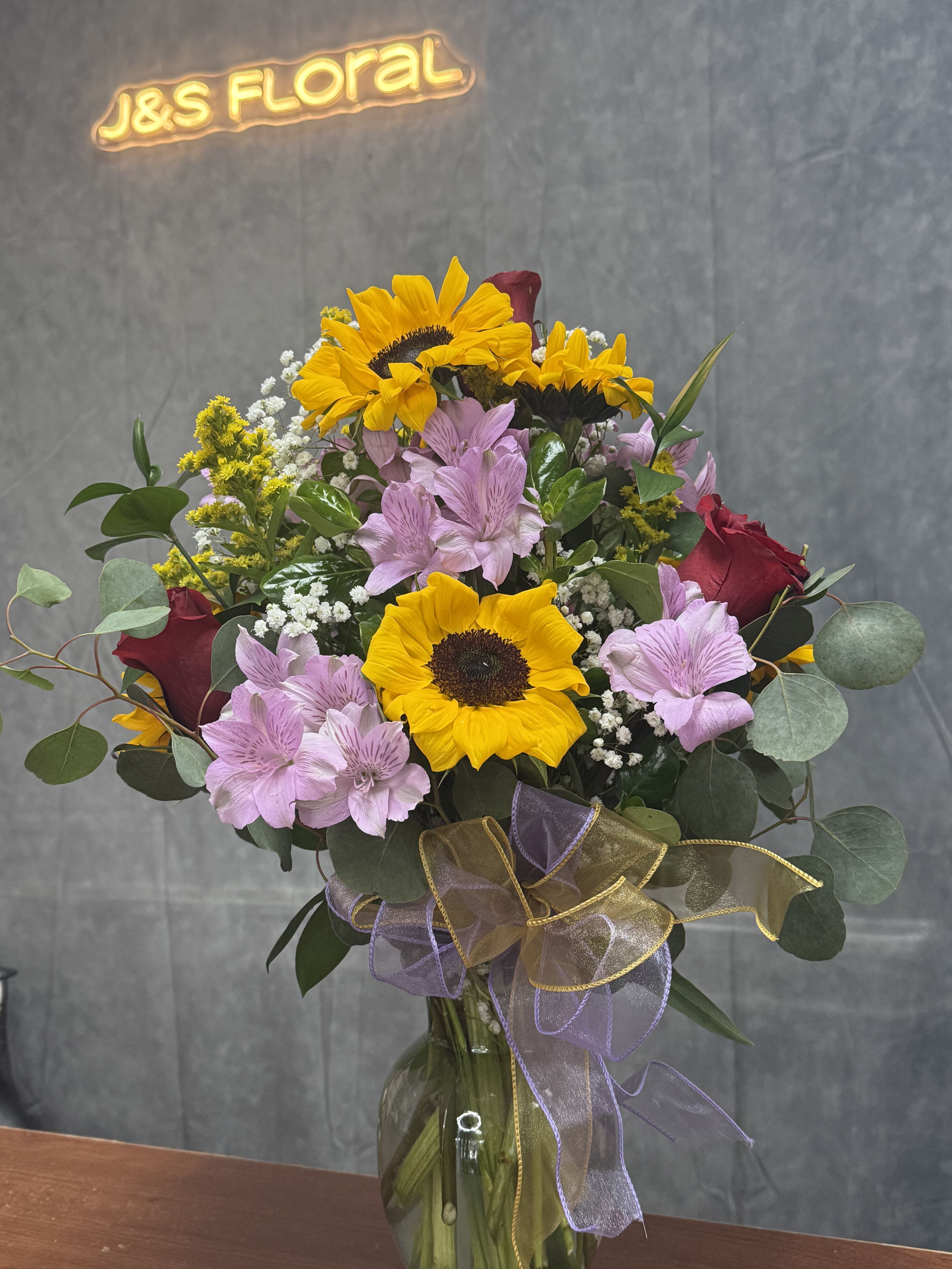 Bouquet of sunflowers, pink alstroemeria, and red roses in a glass vase