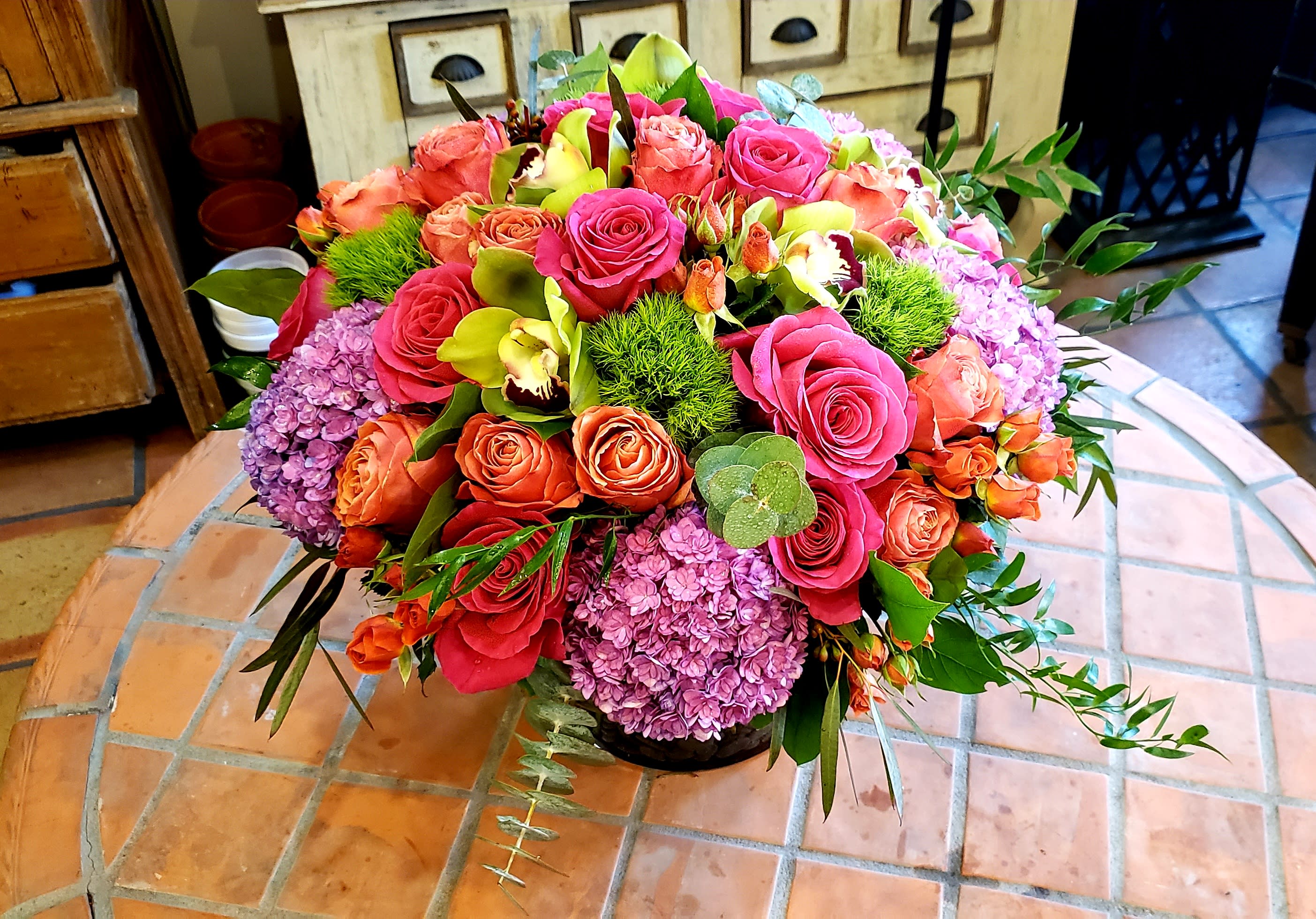 Mixed bouquet of pink and orange roses with purple hydrangeas in a low container
