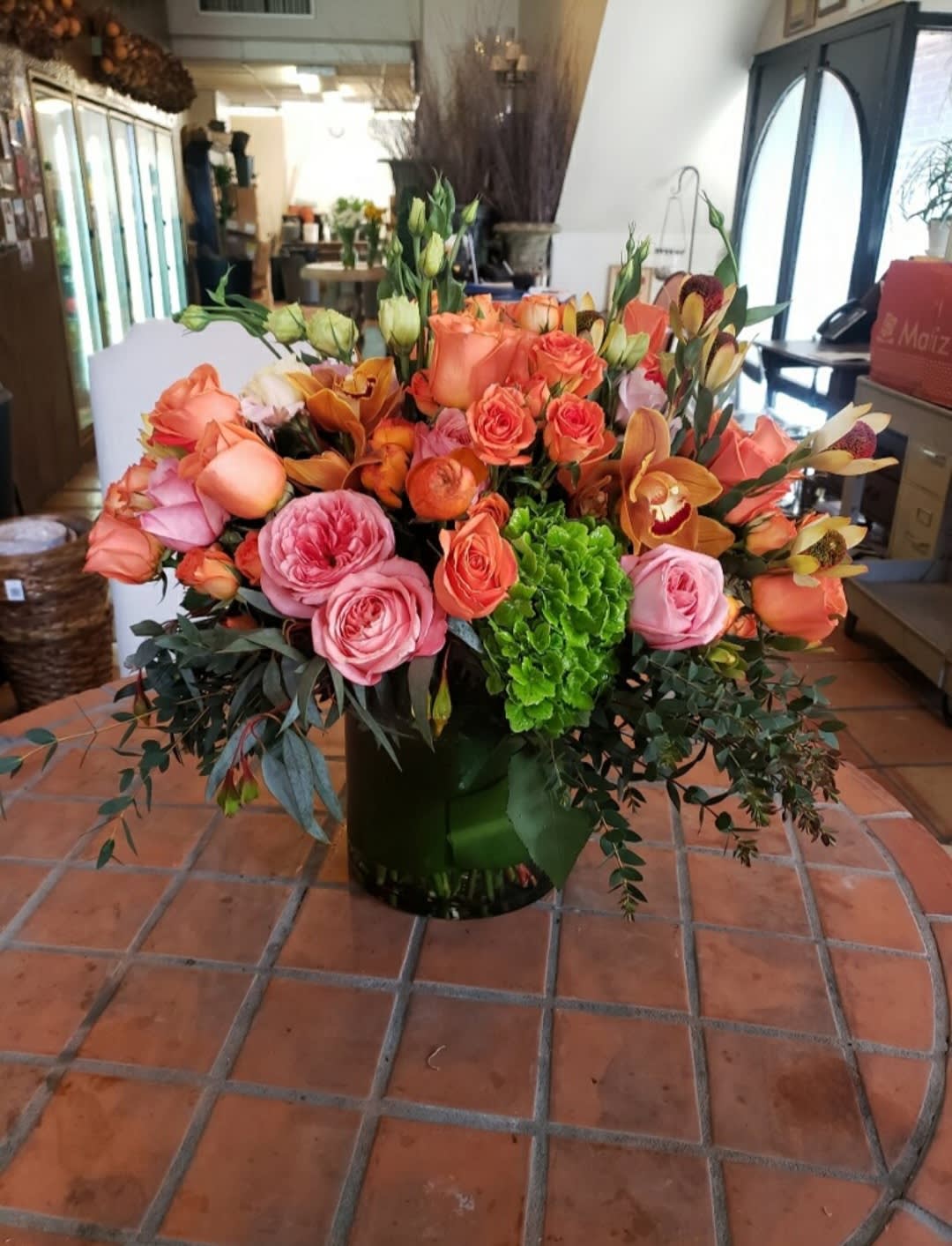Large bouquet of peach and pink roses with orange orchids in a vase