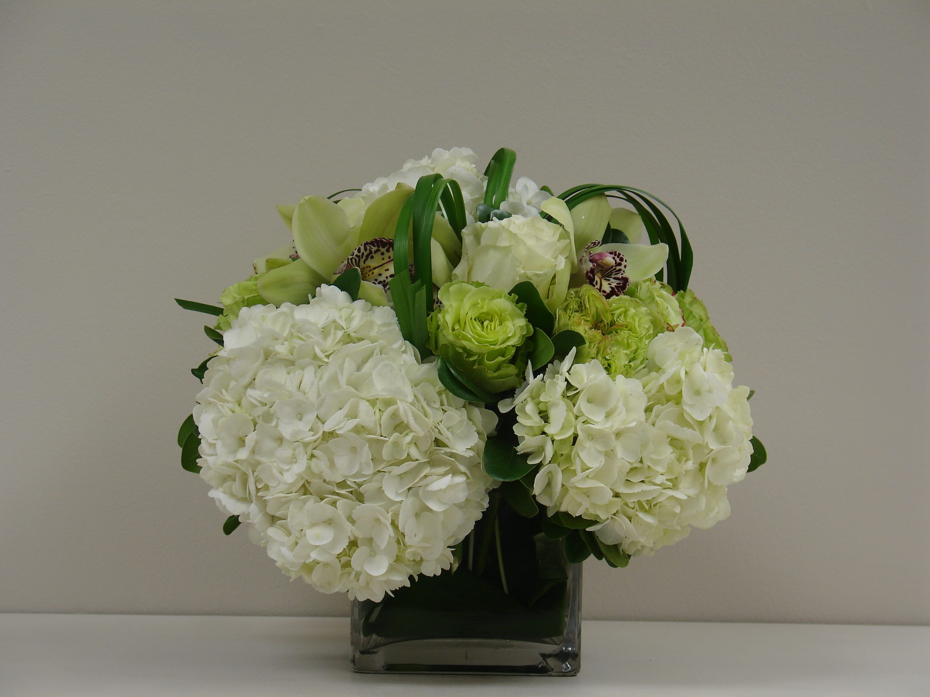 White hydrangeas and green orchids in a square glass vase