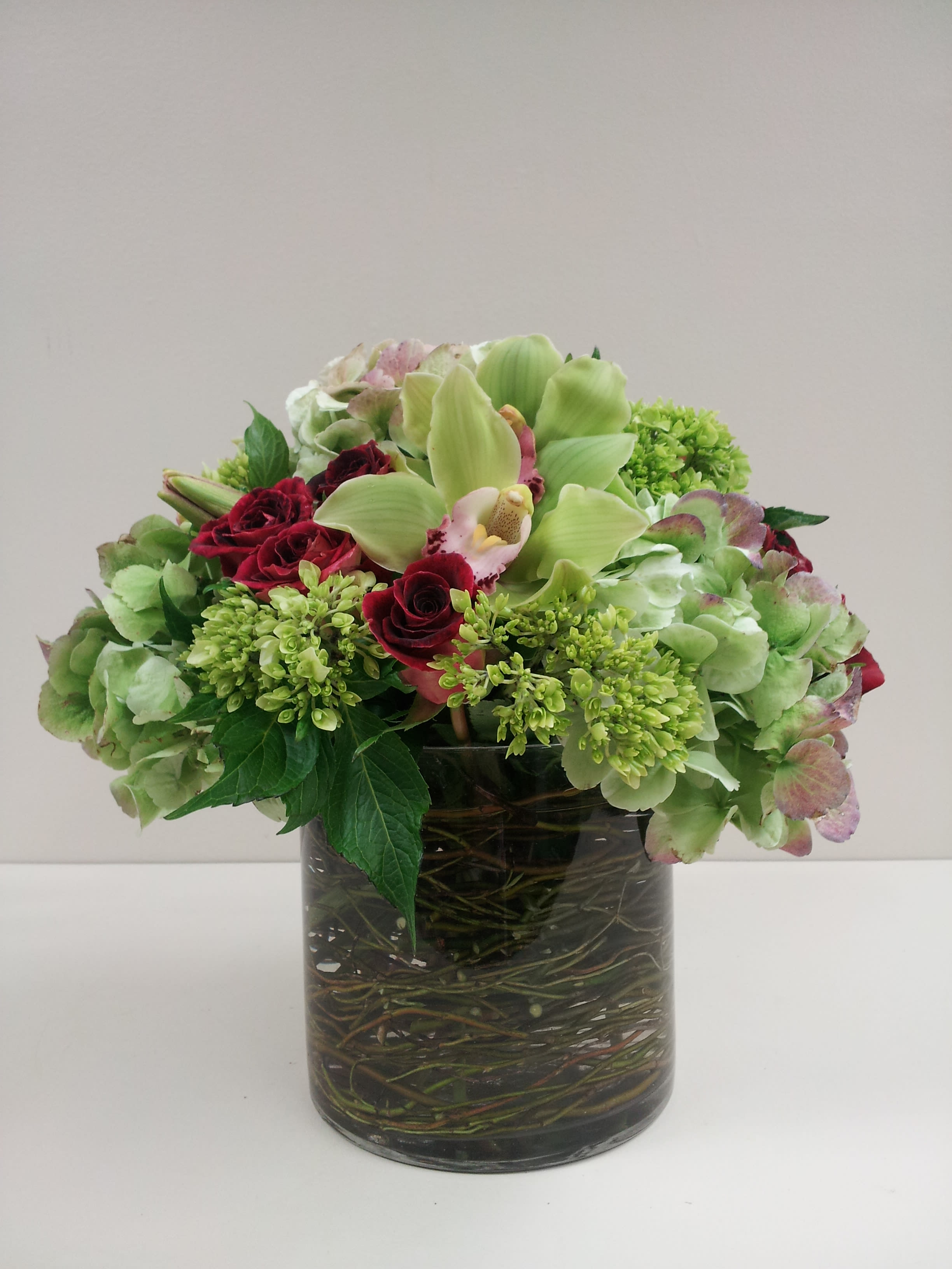Mixed green and burgundy flowers arranged in a glass vase