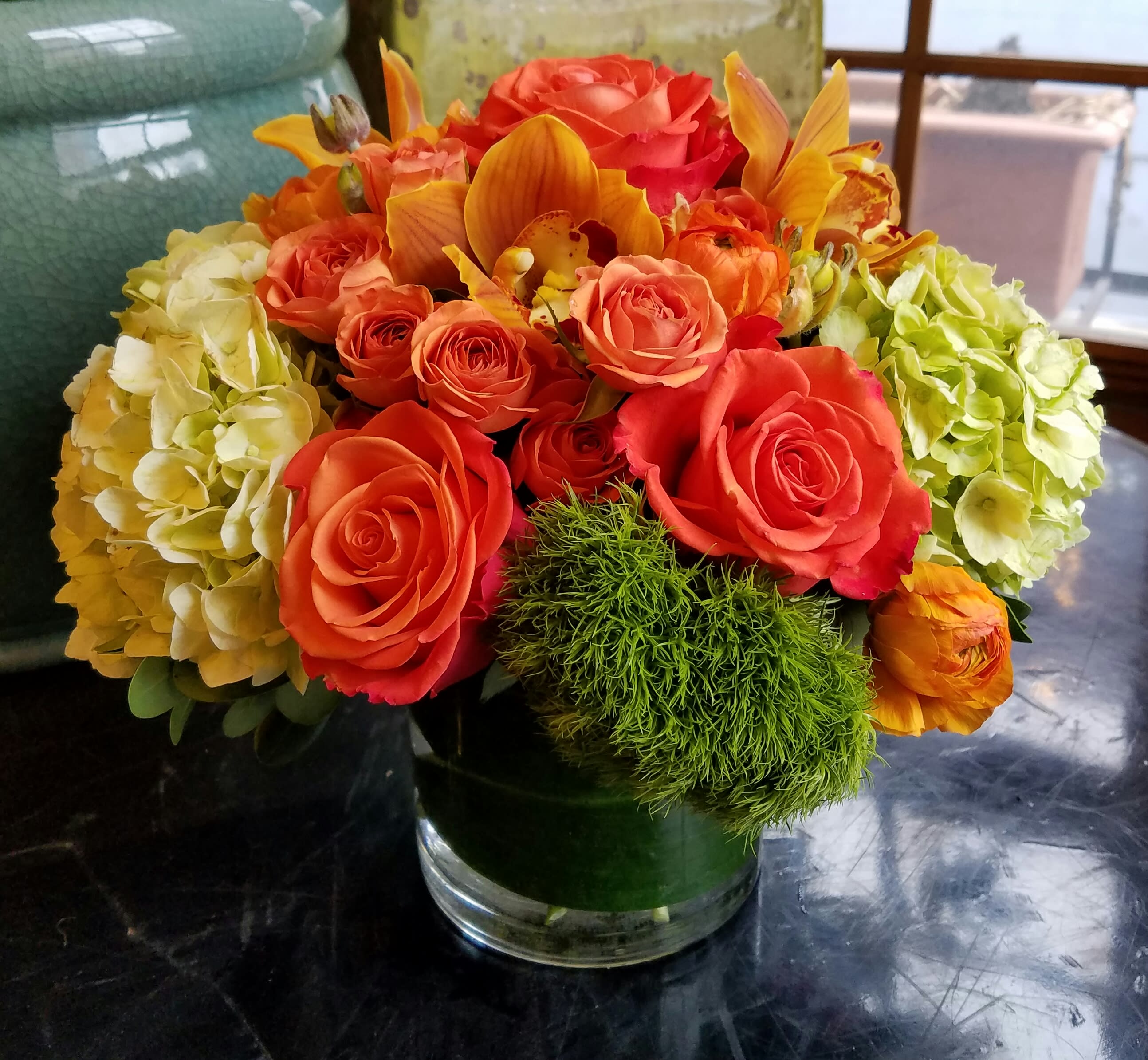 Orange roses and hydrangeas in a glass vase with green accent flowers