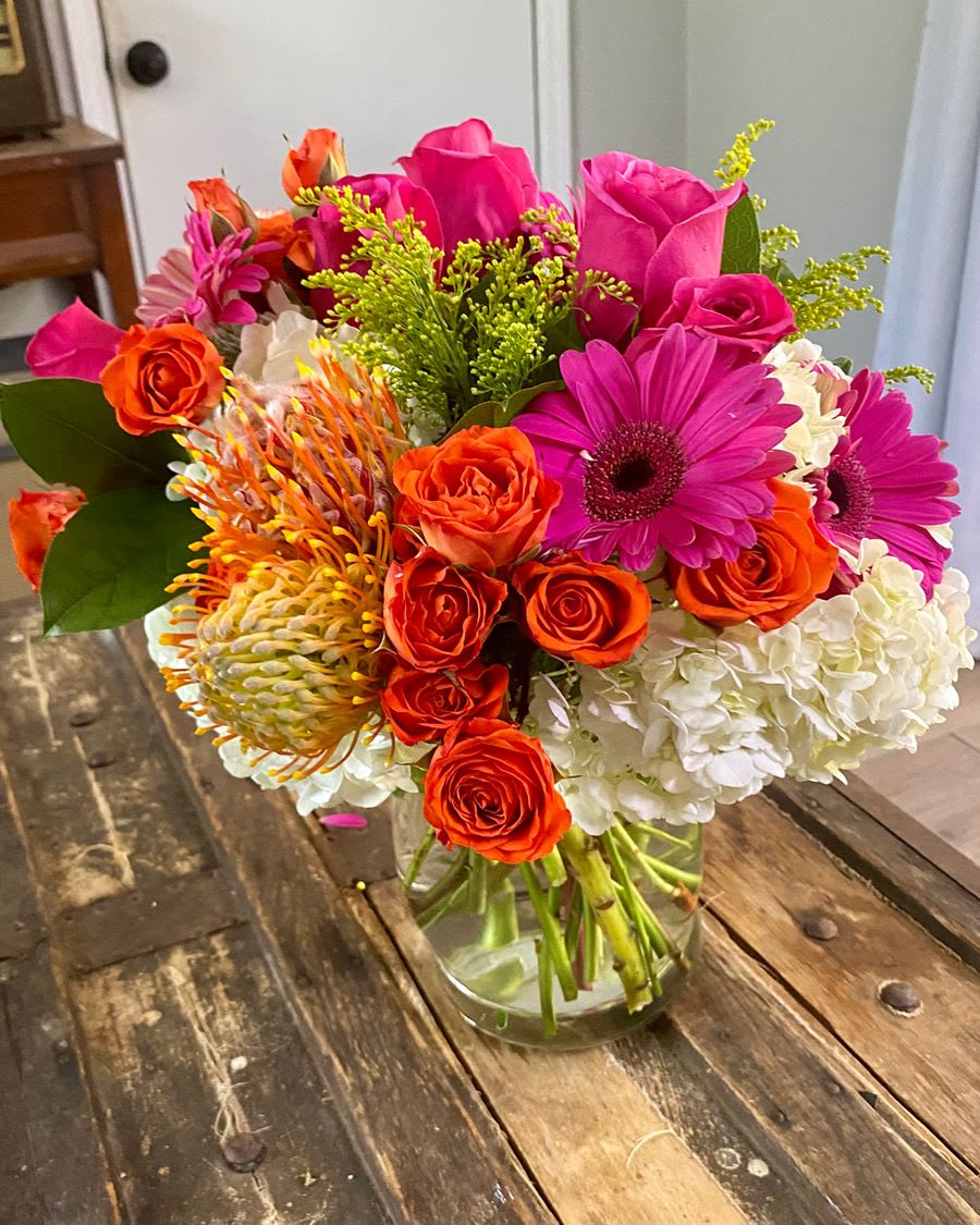 Bright mixed bouquet in a clear glass vase with pink, orange, and white flowers.