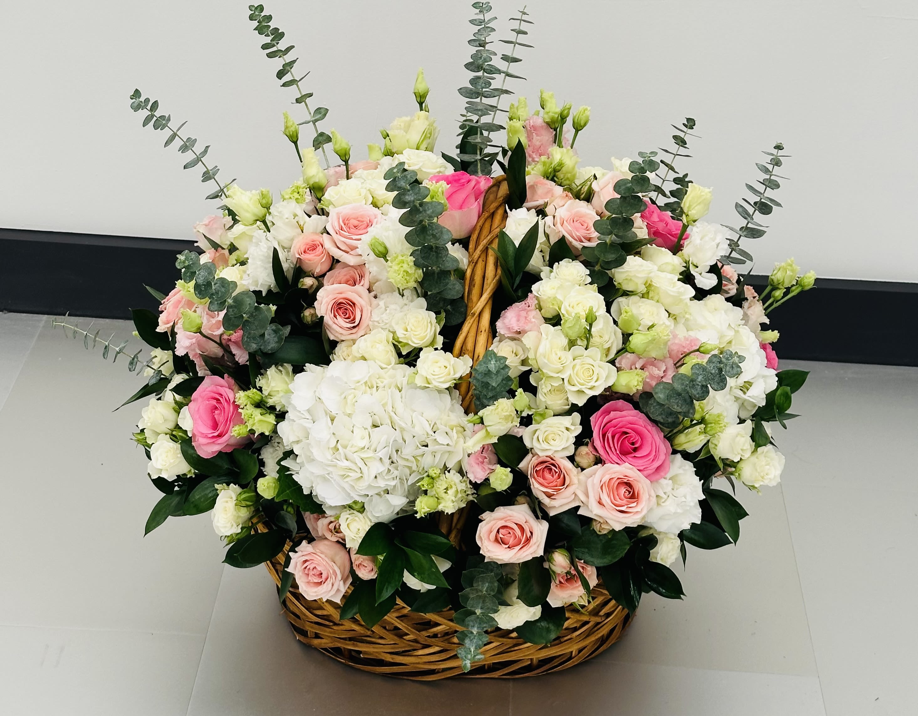Basket arrangement of pink and white roses with hydrangeas and eucalyptus