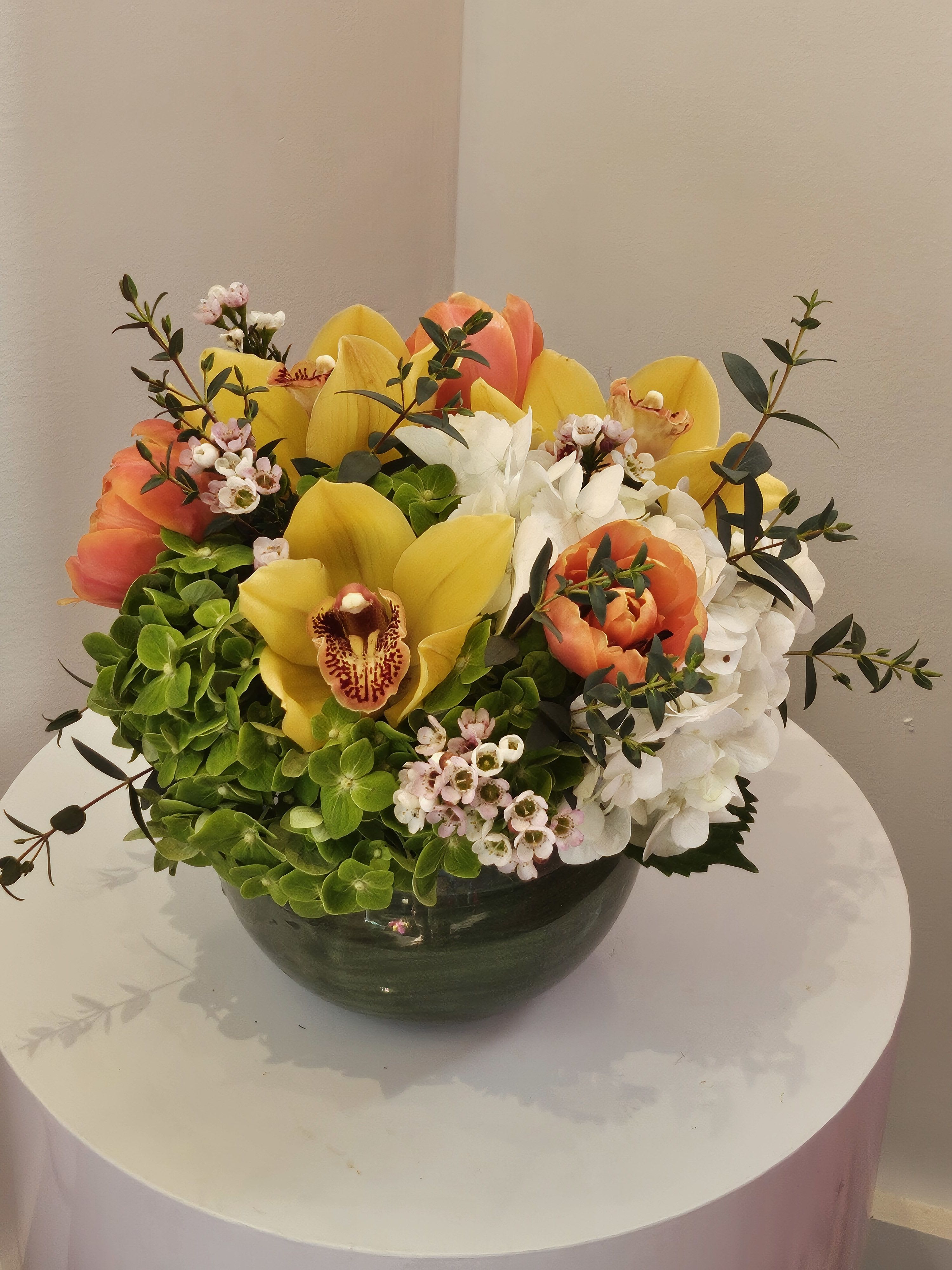 Mixed bouquet of yellow and orange flowers in a dark bowl vase
