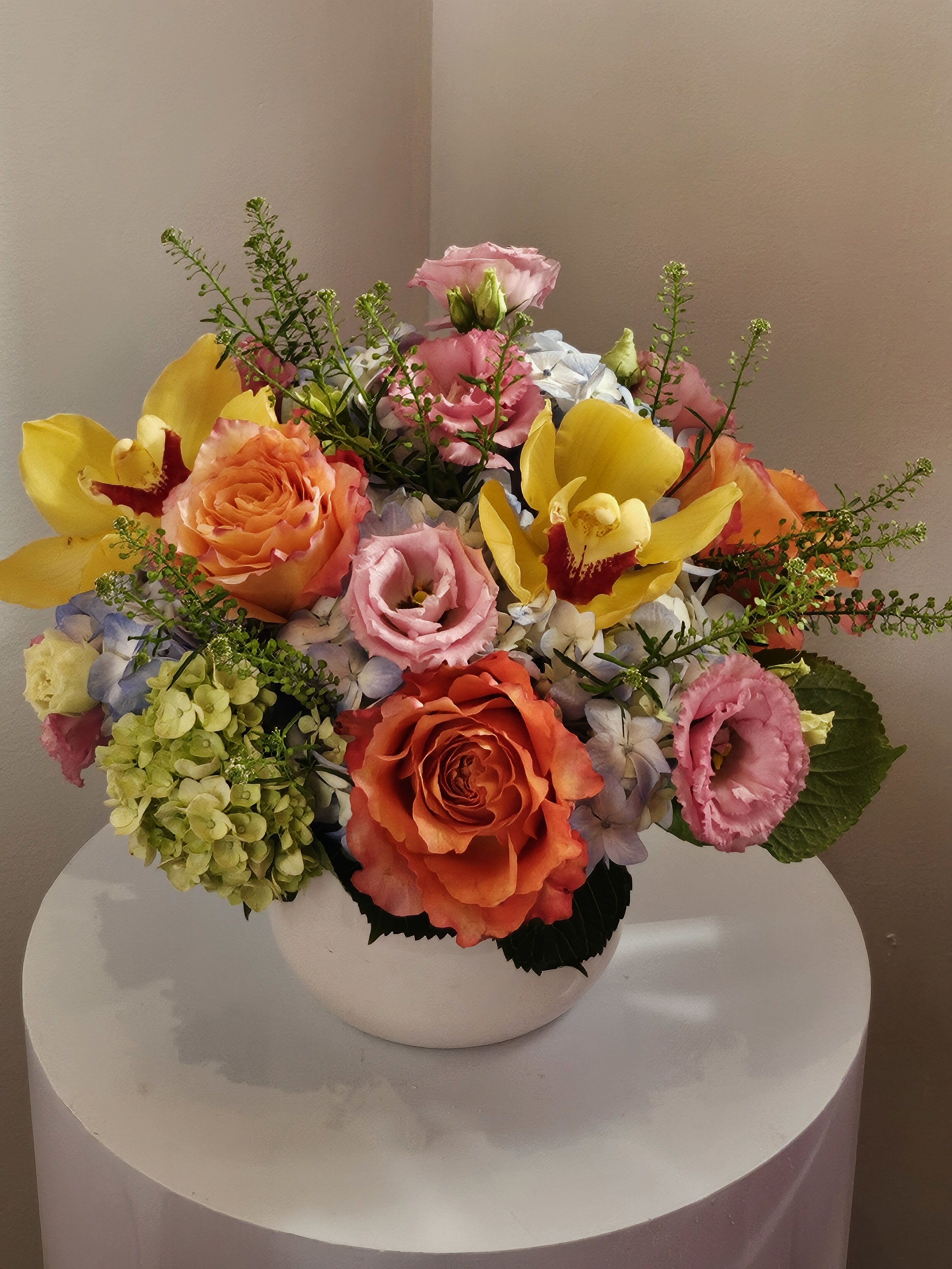 Mixed bouquet of roses, orchids, and hydrangeas in a white vase