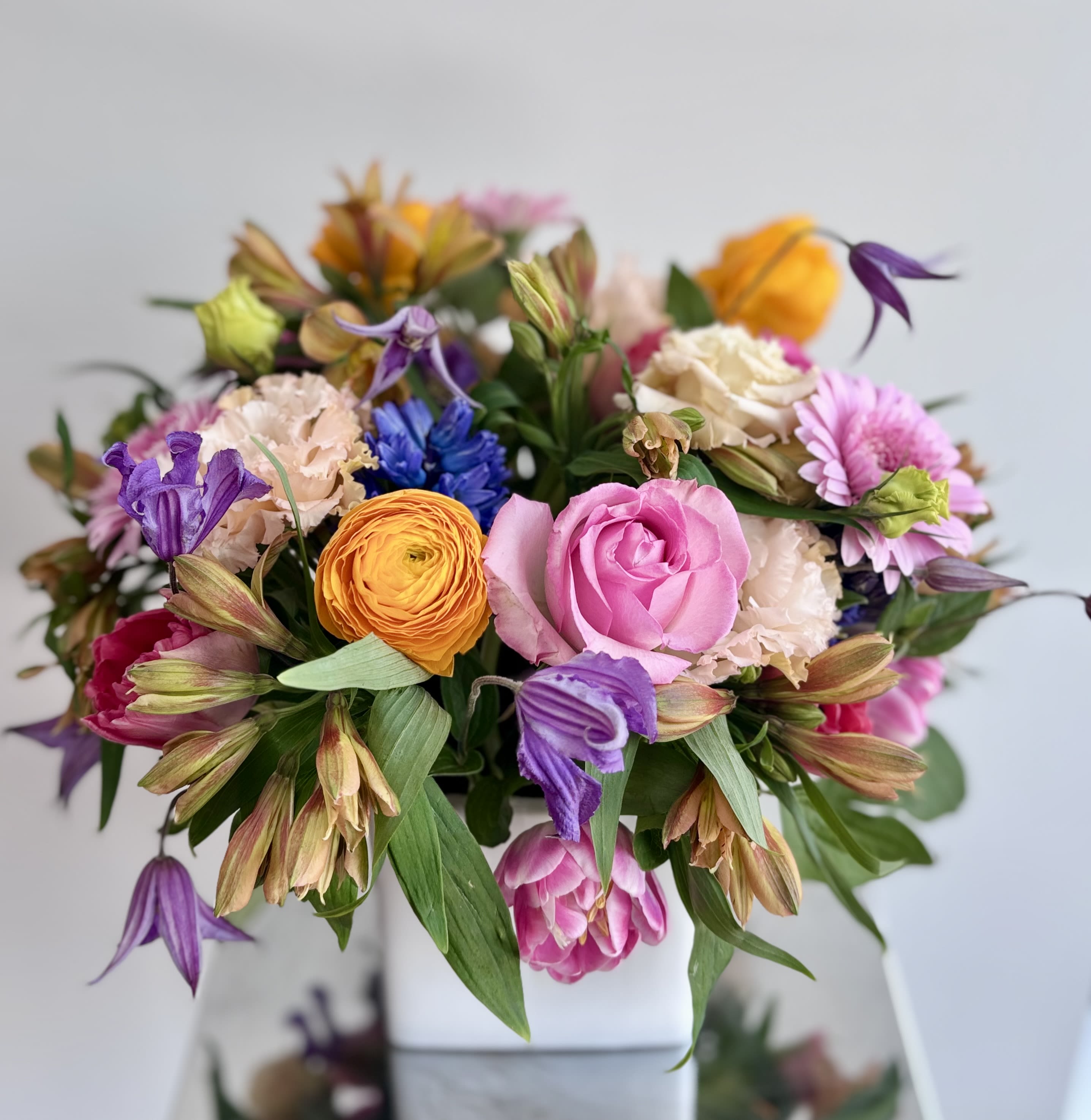 Mixed bouquet of pink, purple, orange, and cream flowers in a white vase
