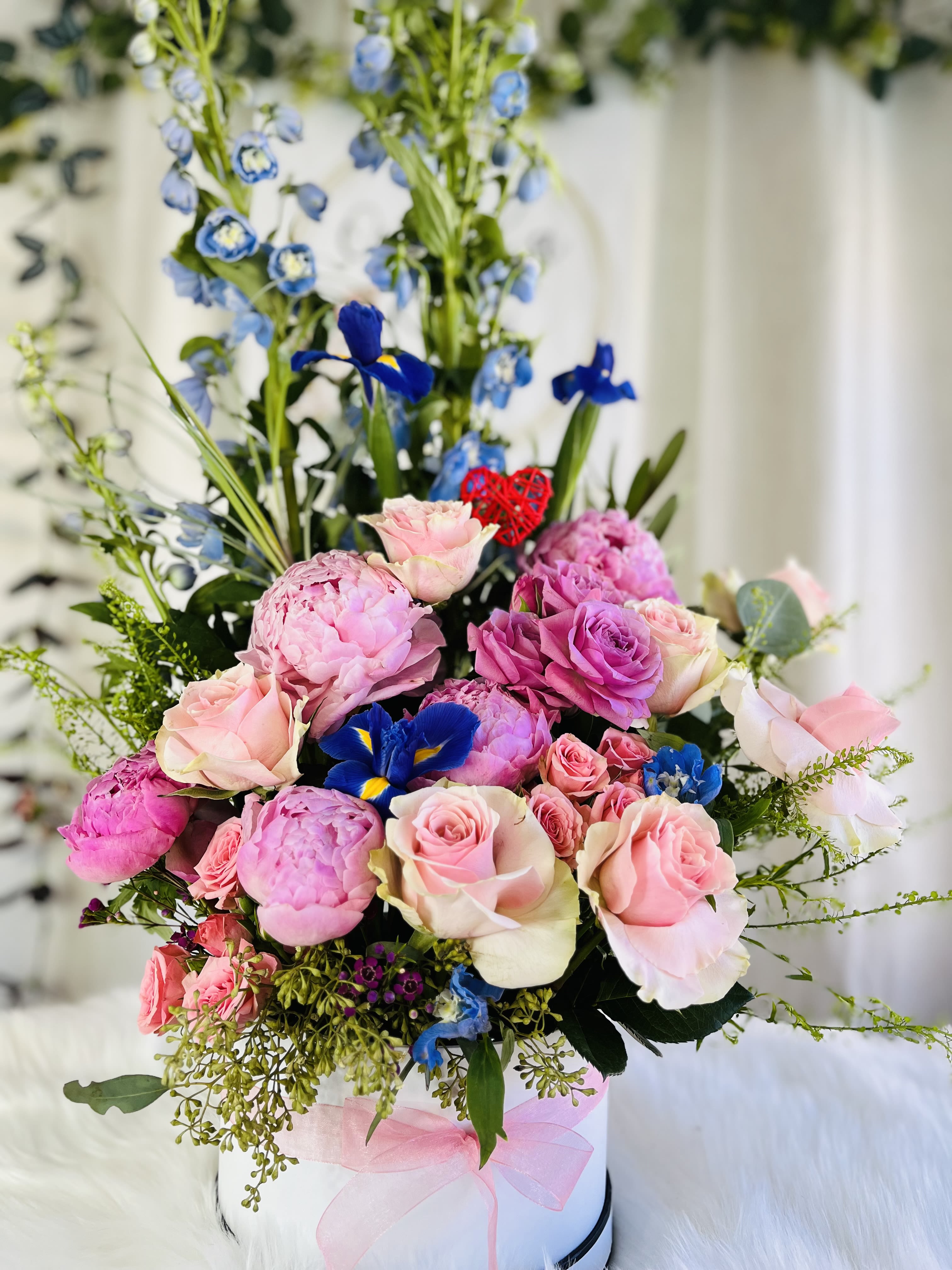 Pink roses and peonies arranged with blue irises in a white hat box