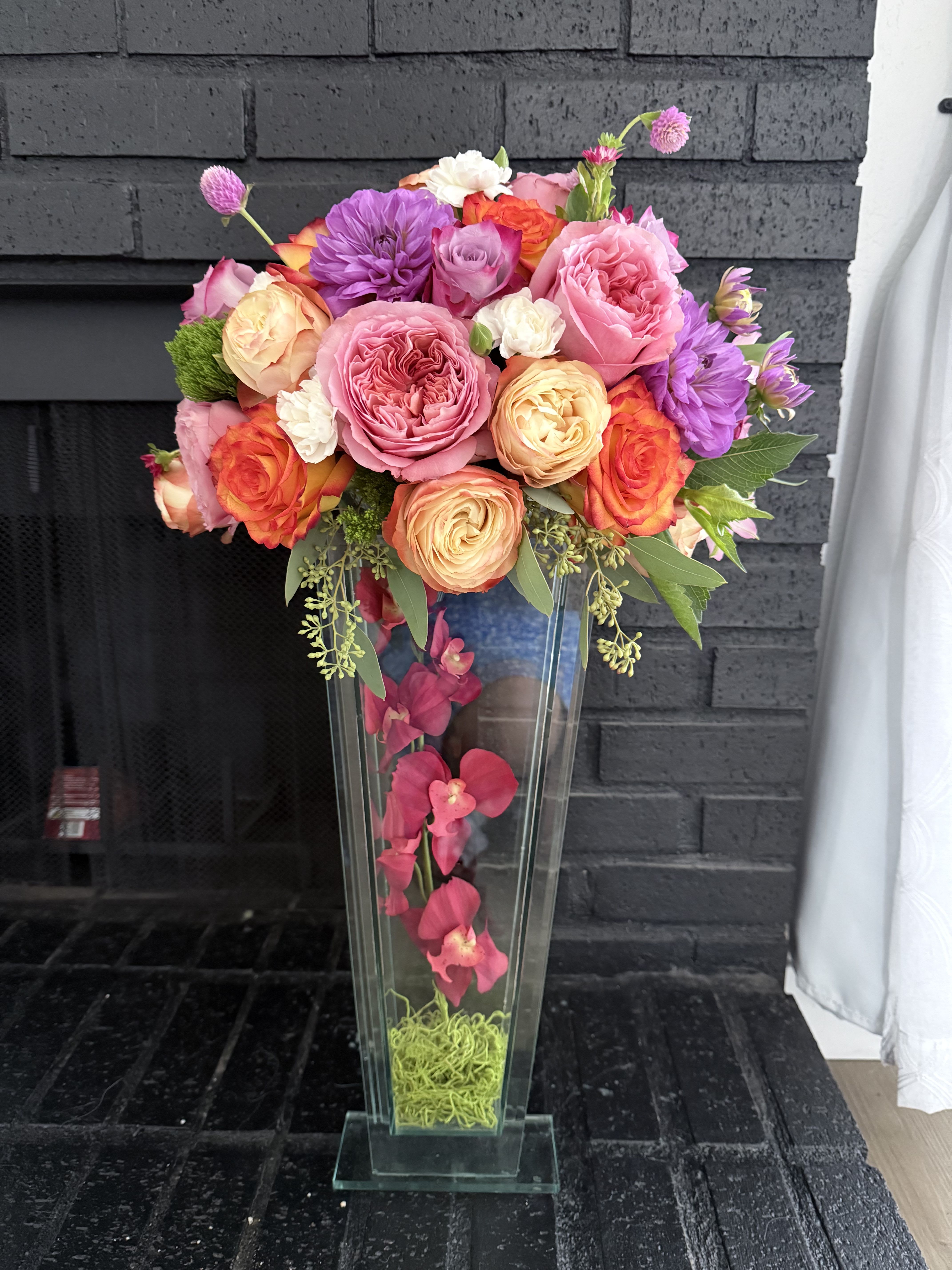 Tall floral arrangement in a clear glass vase with pink, orange, and purple blooms