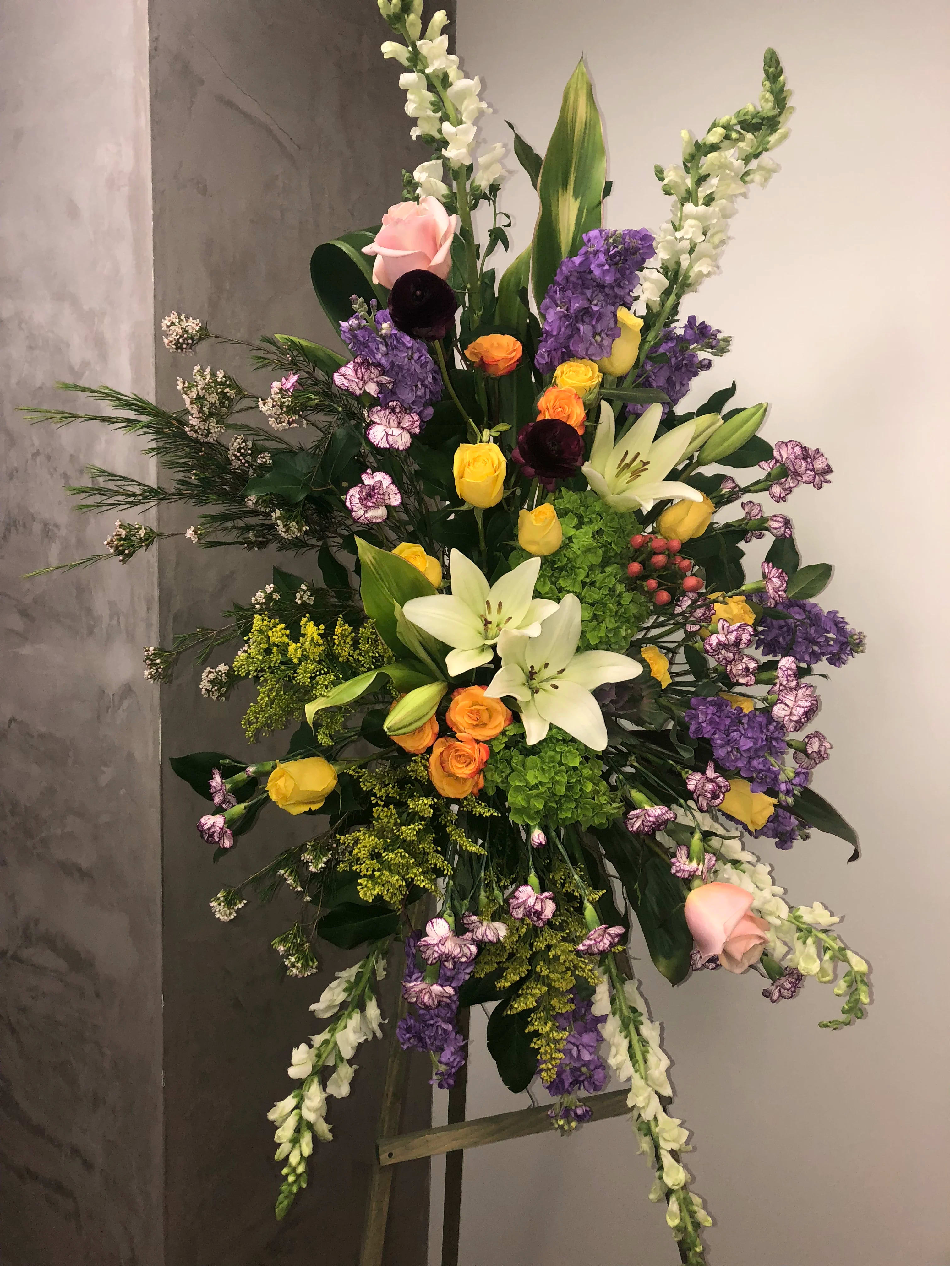 Blooms of The Soul - A nice way to say farewell to a loving soul that you will always remember and talk about. A  gorgeous standing spray appropriate for a man or woman with white lilies,yellow and orange roses,lavender stock,white snapdragons and pretty greens.