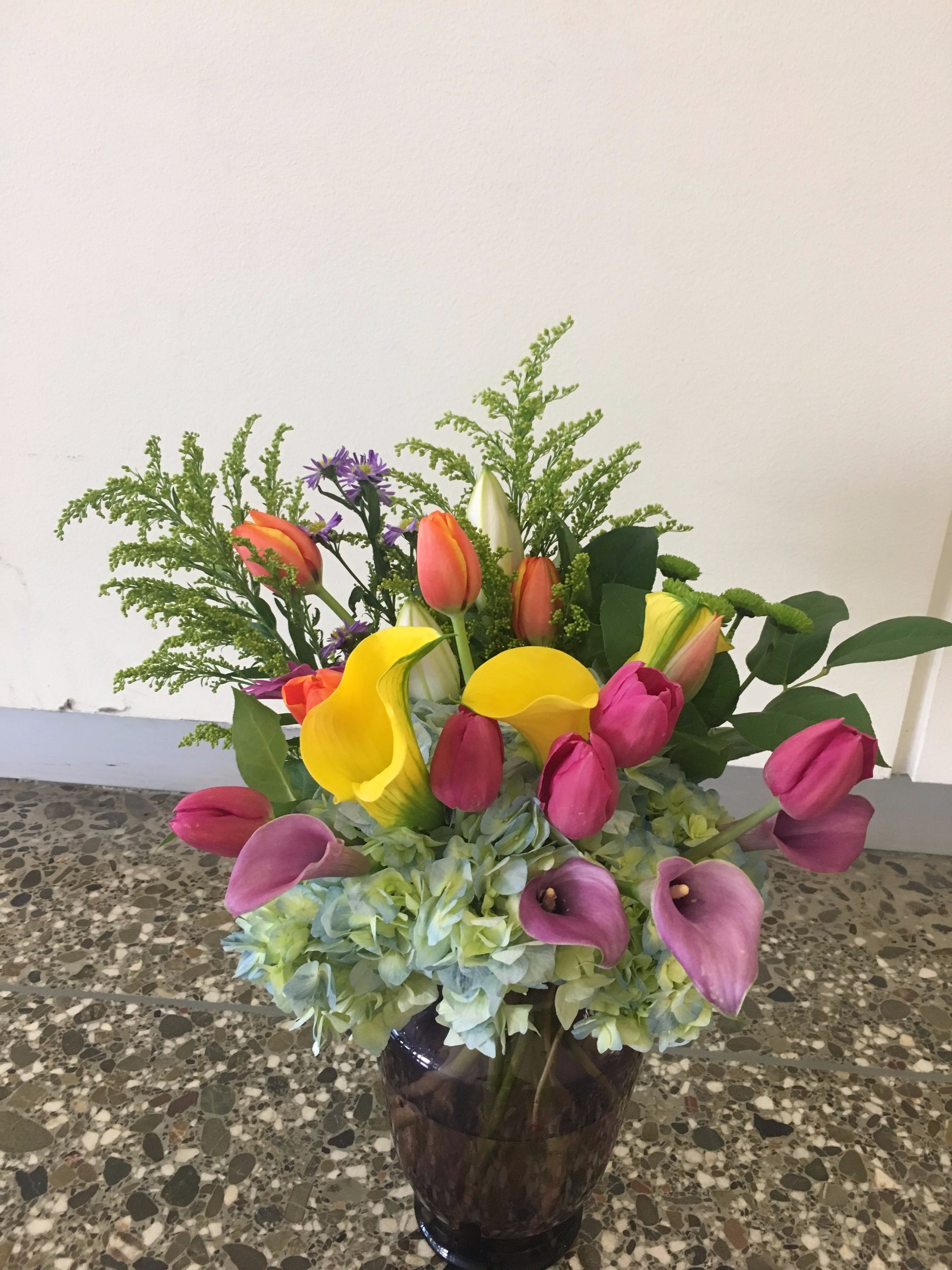 Colorful bouquet with tulips, calla lilies, and hydrangeas in a dark vase