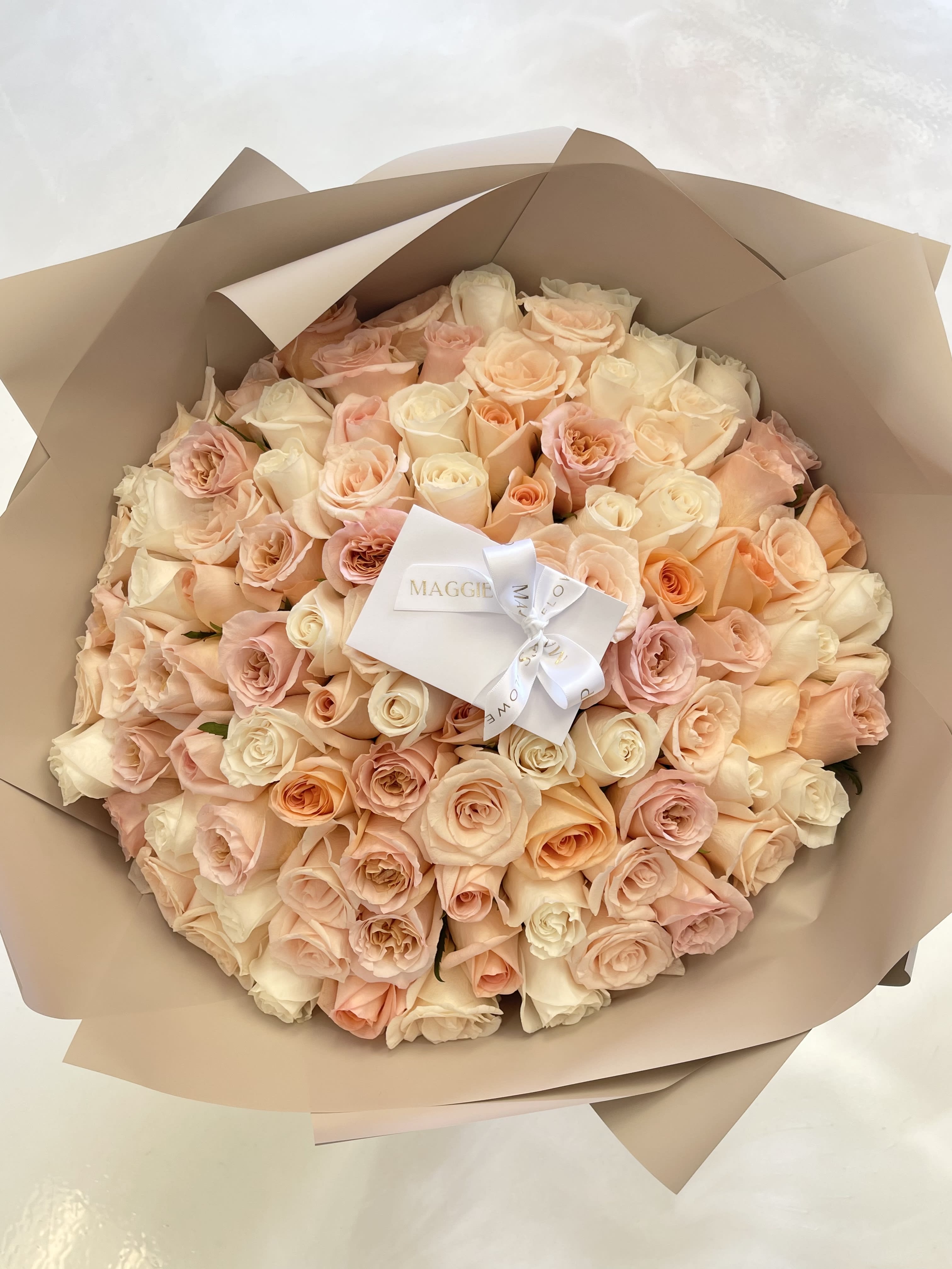 Bouquet of blush and cream roses wrapped in tan paper with a white ribbon