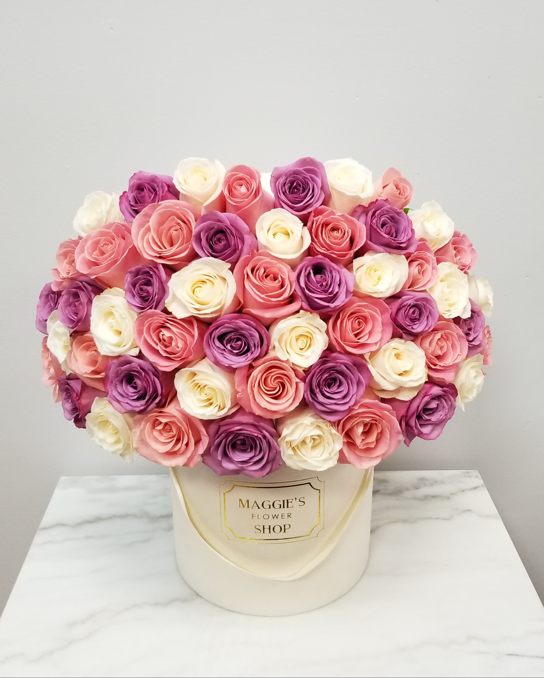 Round bouquet of pink, purple, and white roses in a cream hat box