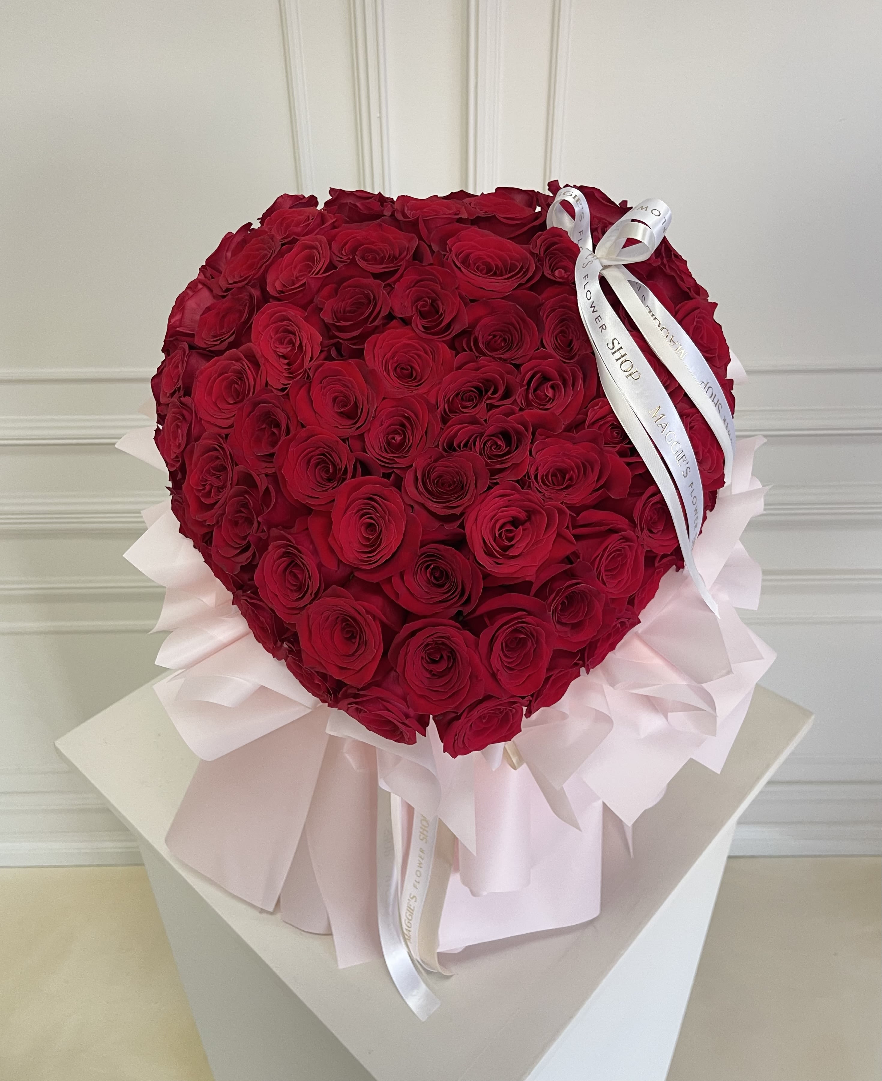 Heart-shaped bouquet of red roses with pale pink wrapping and white ribbon