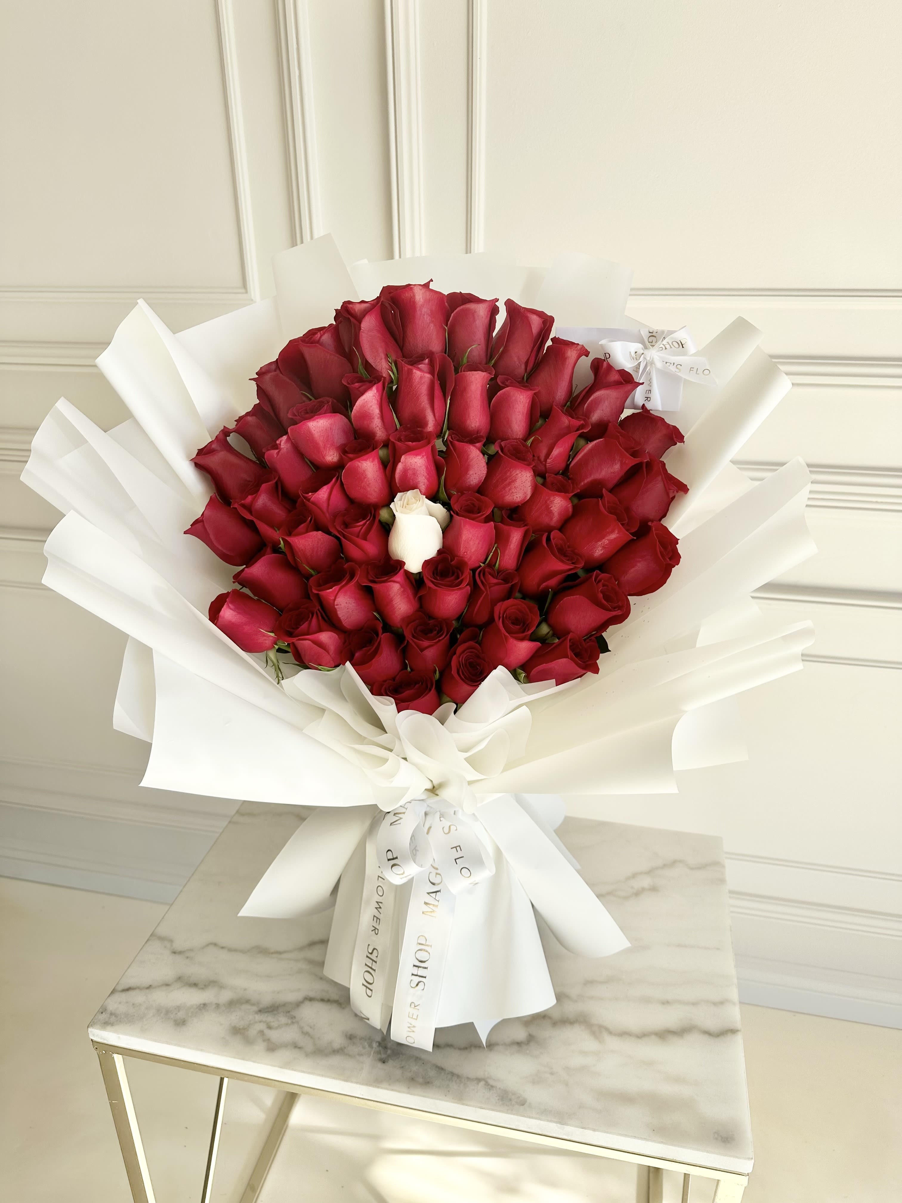 Bouquet of red roses wrapped in white paper with one white rose