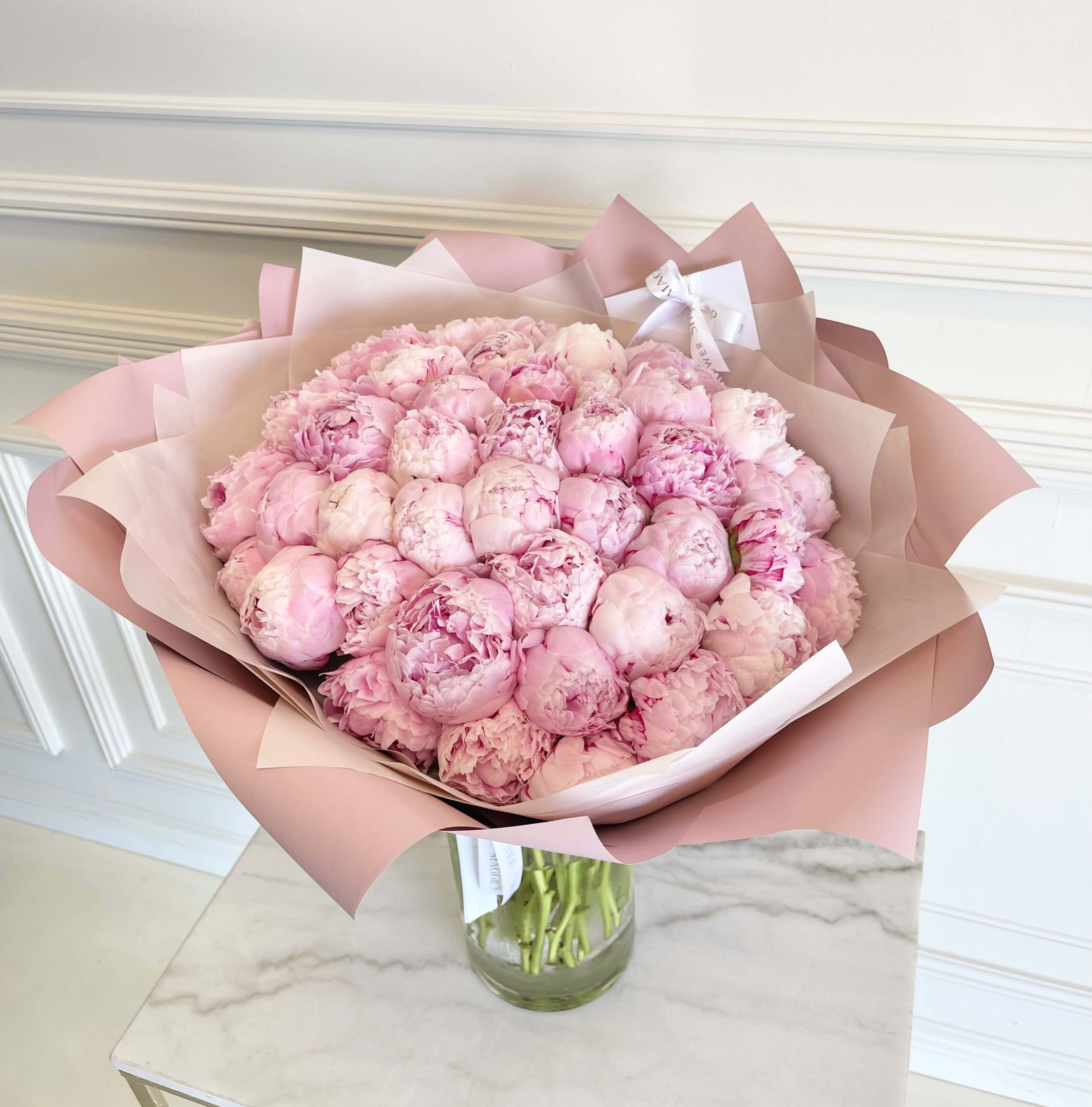 Bouquet of pale pink peonies wrapped in blush paper in a glass vase