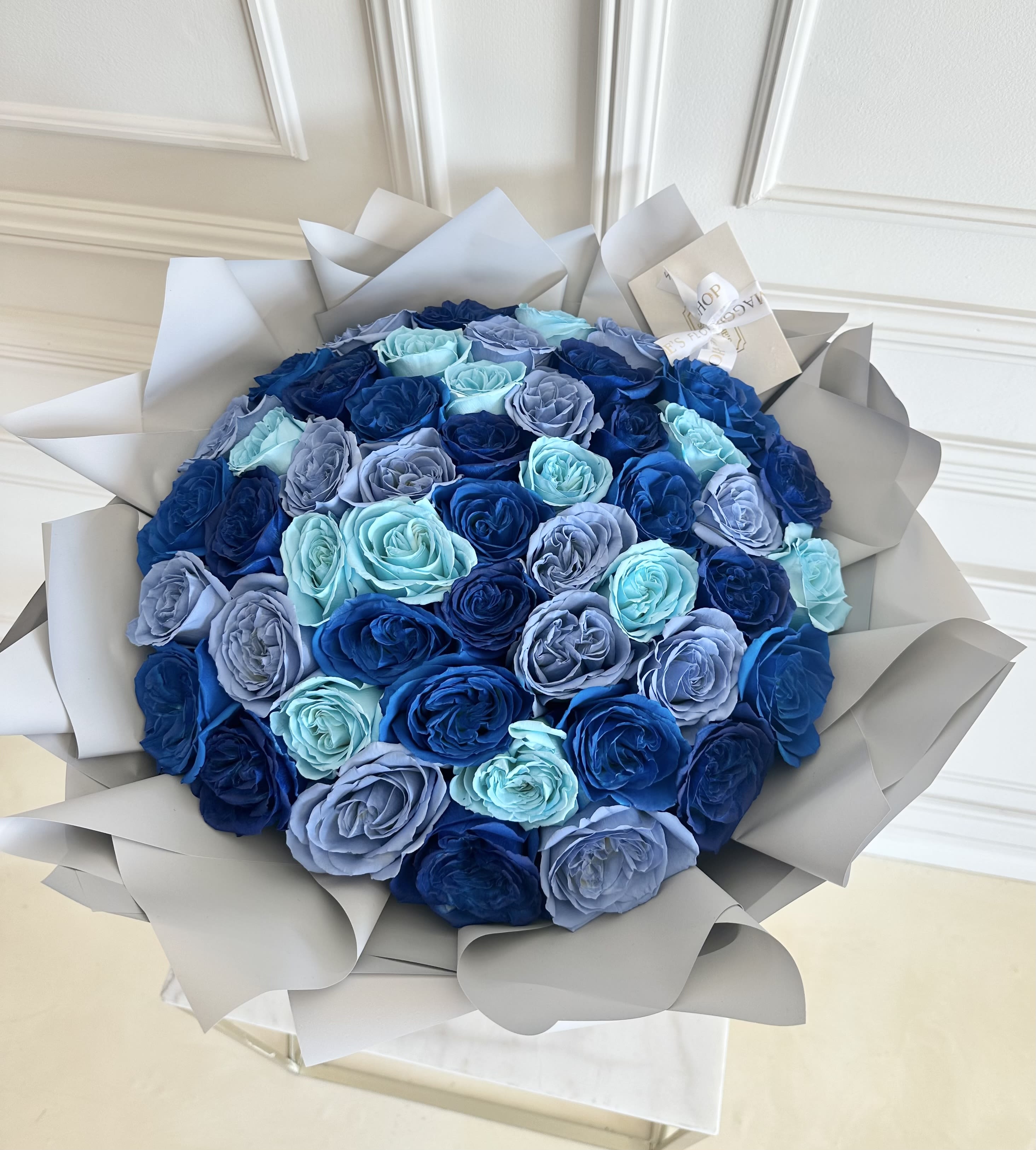 Round bouquet of blue and lavender roses wrapped in pale paper