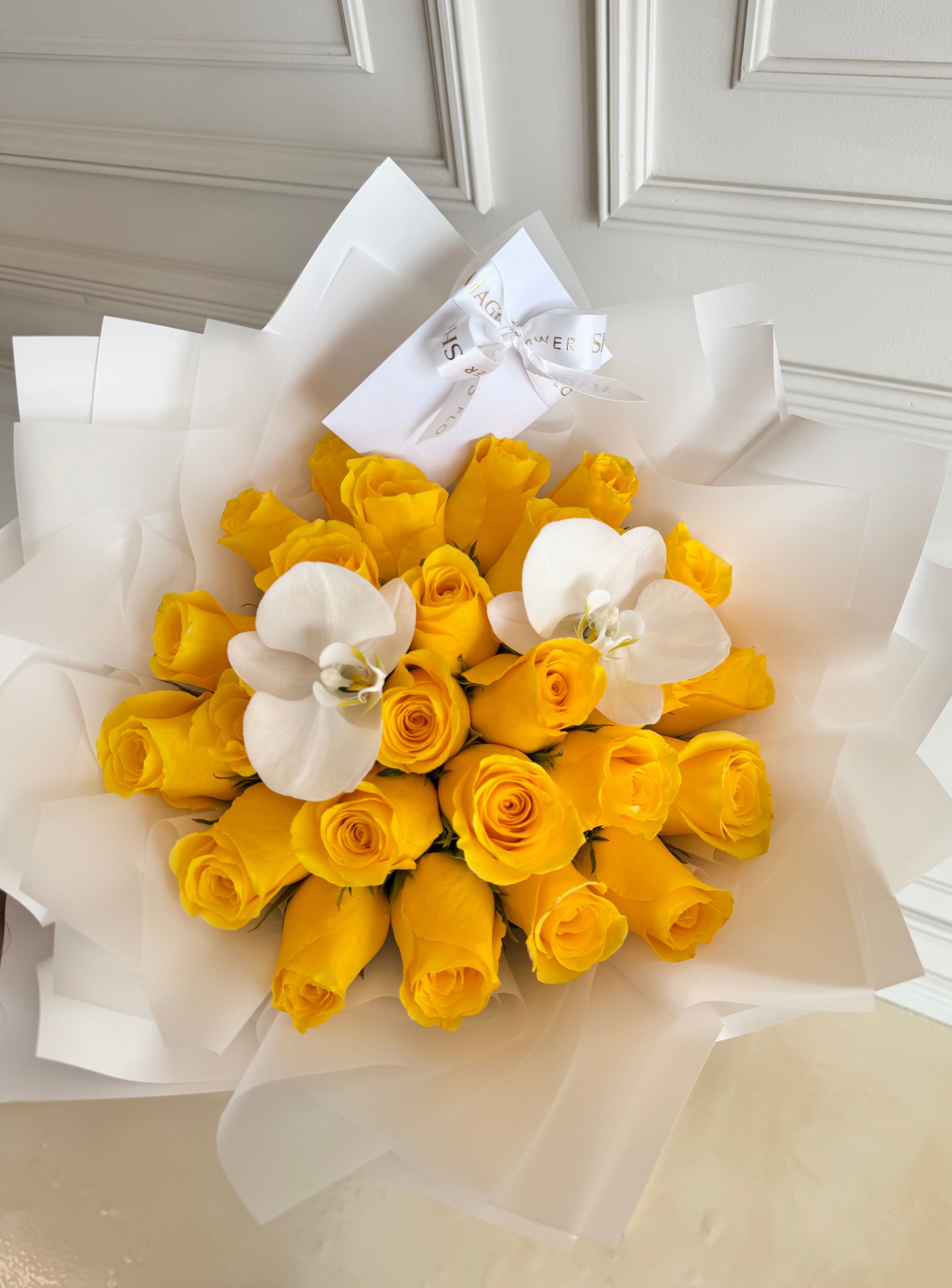 Bouquet of yellow roses with two white orchids wrapped in white paper