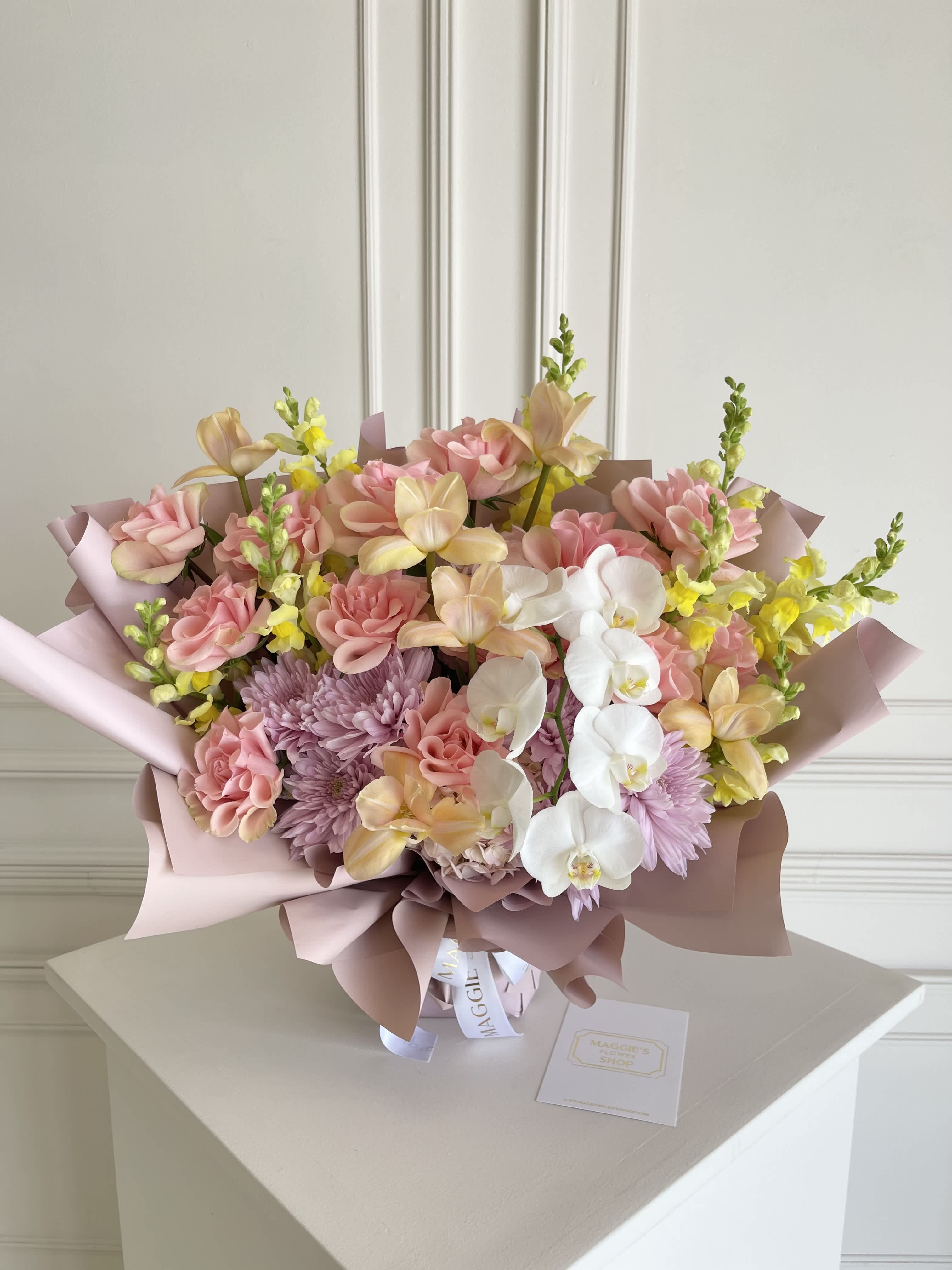 Pastel bouquet with pink roses, orchids, and lavender mums wrapped in blush paper