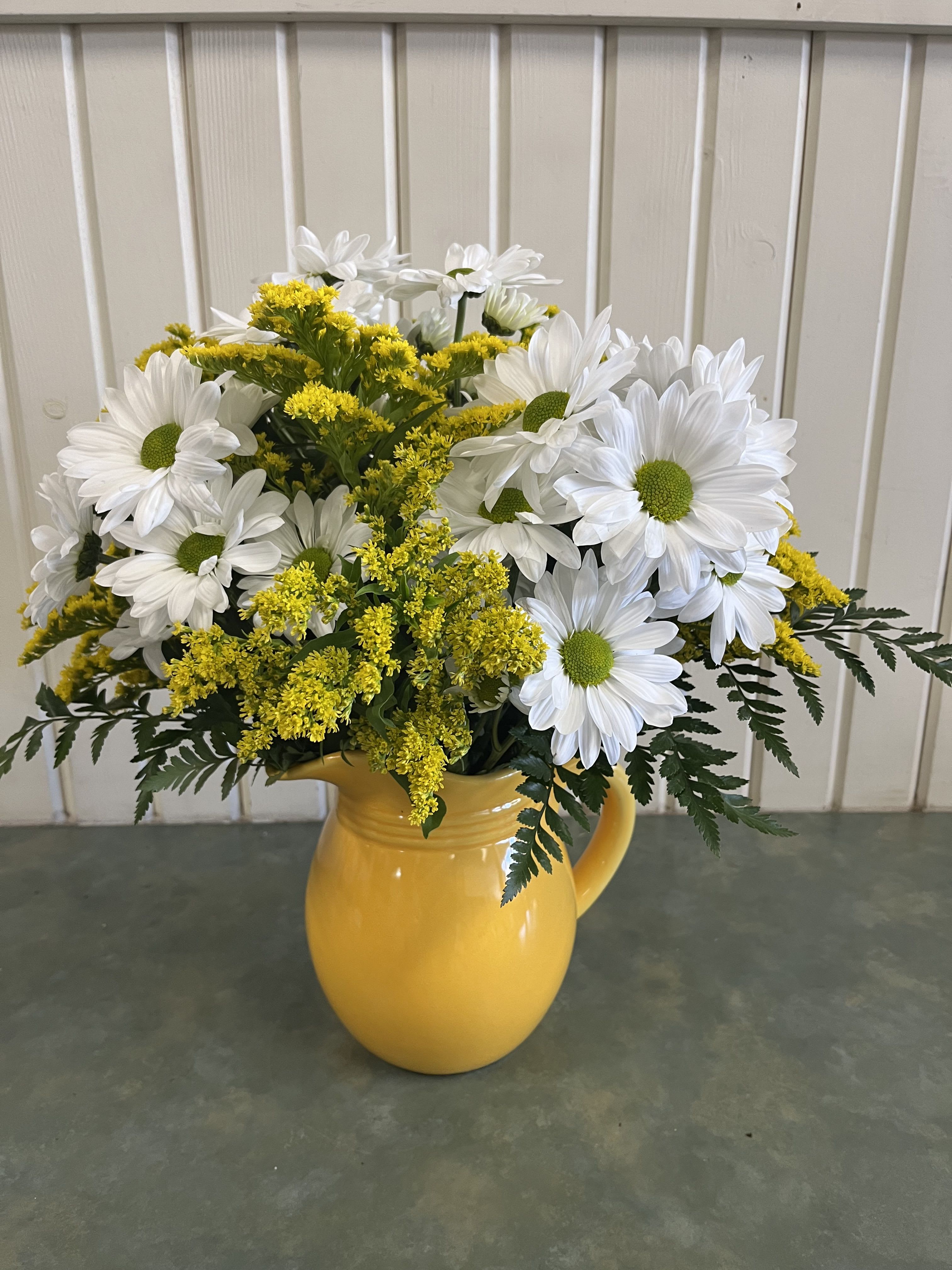 White daisies and yellow filler flowers in a yellow pitcher vase
