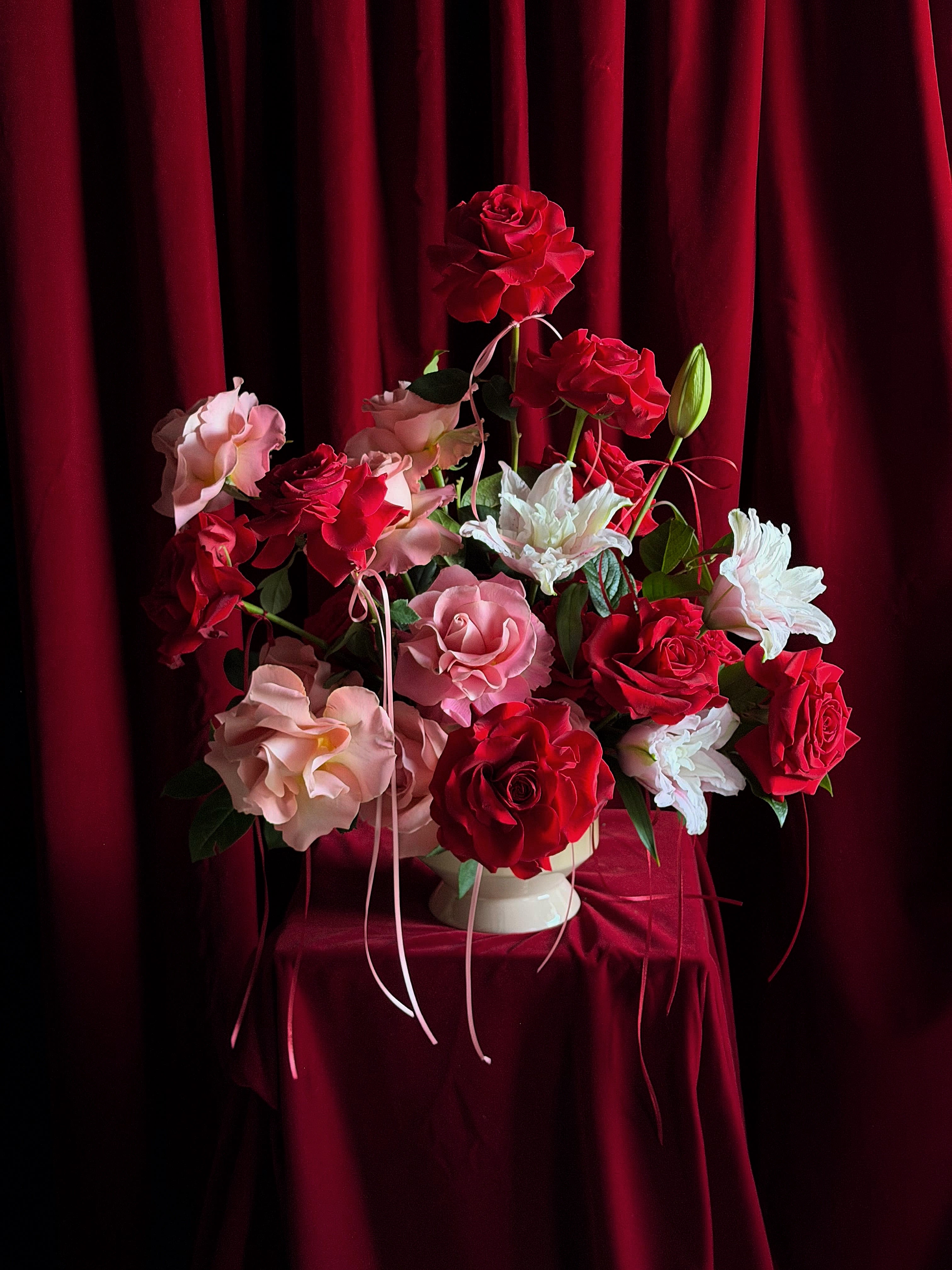 Red and pink roses arranged in a white vase against a burgundy backdrop
