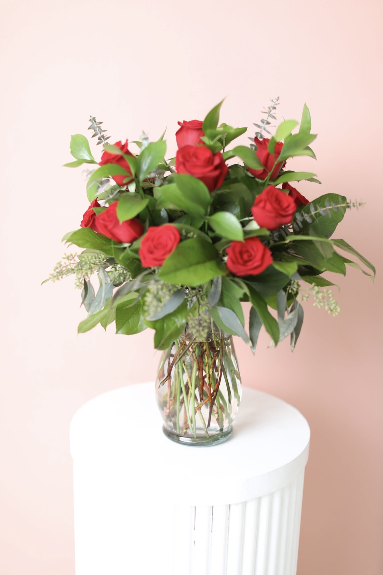 Red roses arranged in a clear glass vase with greenery