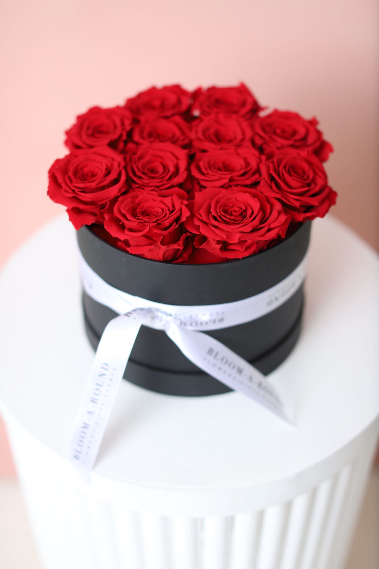 Red roses arranged in a black round box with a white ribbon