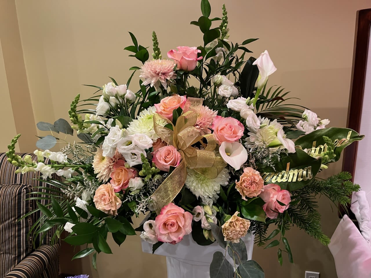 Large pink and white floral arrangement with a gold ribbon in a white pedestal vase