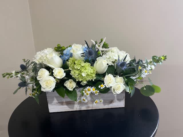 White roses and hydrangeas arranged in a wooden box with blue thistle accents.