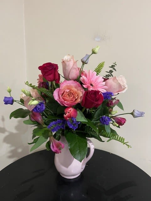Mixed pink, red, and purple flowers arranged in a pale pitcher vase