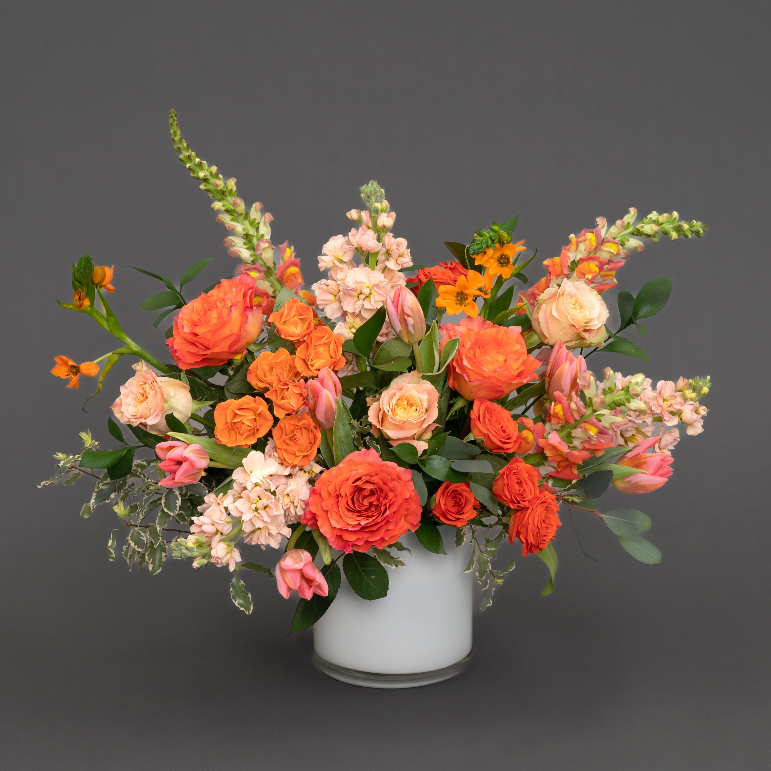 Orange and blush mixed flower arrangement in a white vase