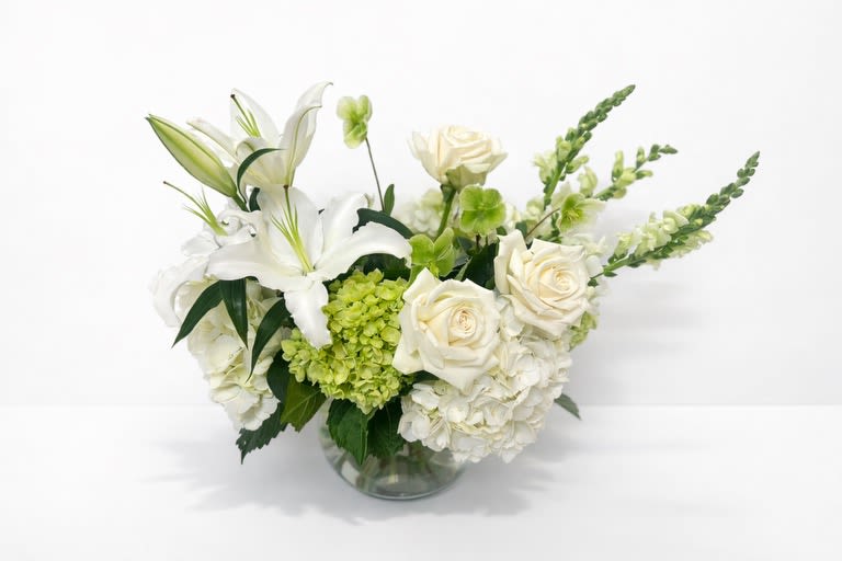 White lilies and roses in a clear glass vase with green accents
