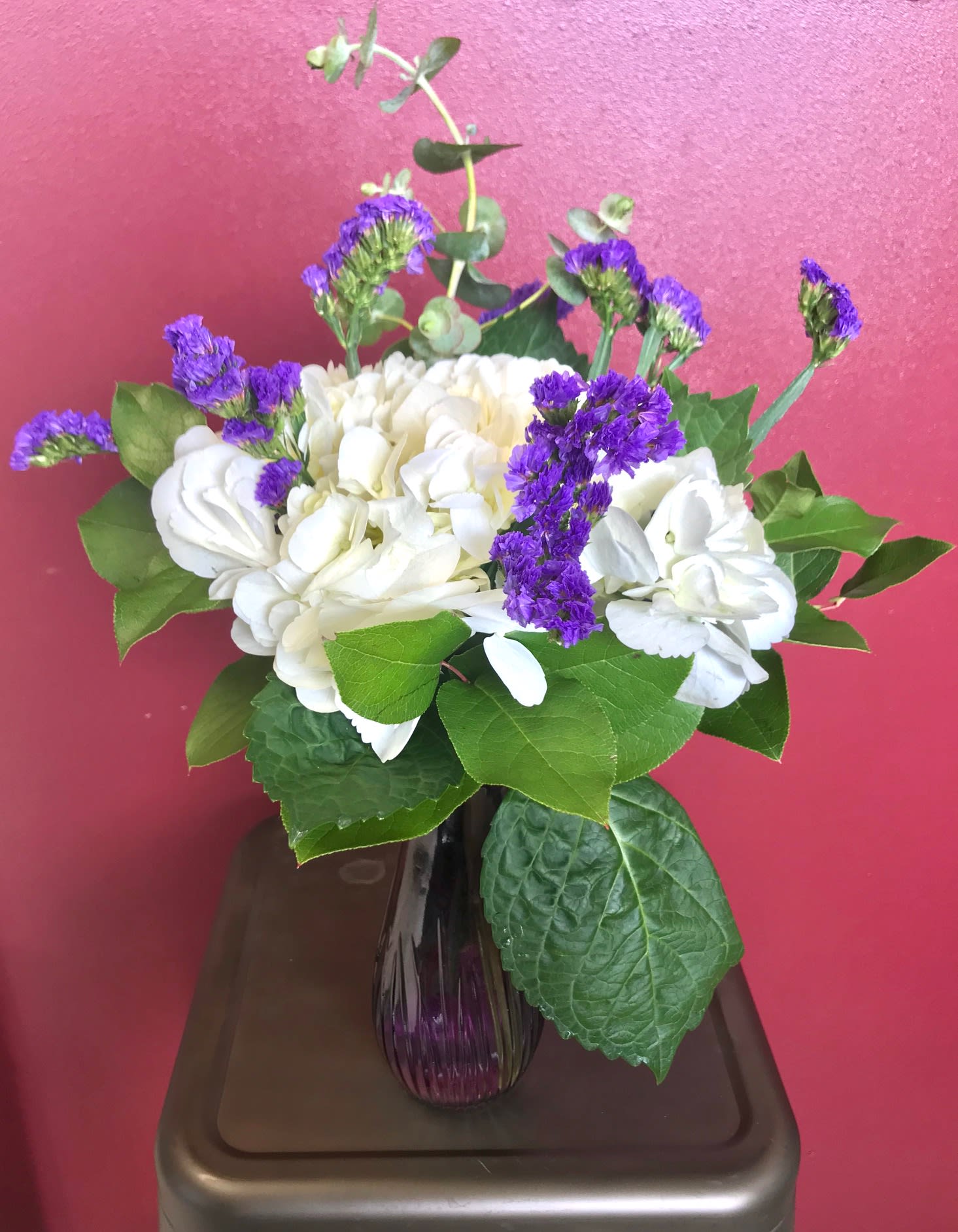 White hydrangeas and purple filler flowers in a glass vase