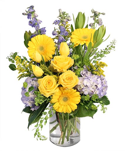Yellow roses and gerbera daisies with purple flowers in a glass vase