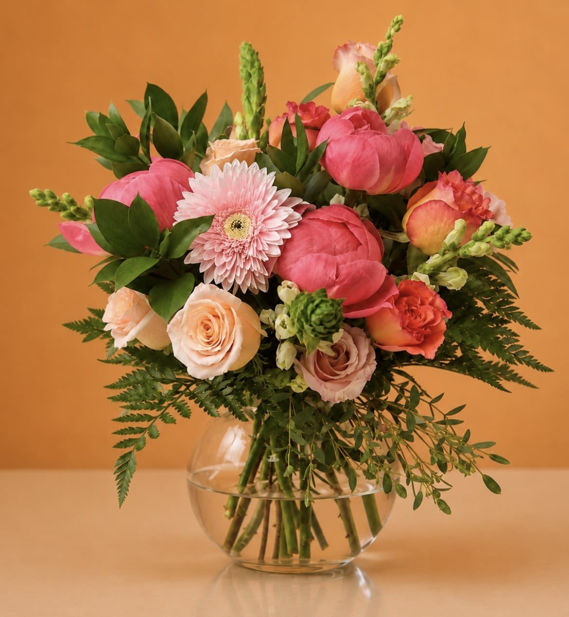 Peony Pop – Weekly Floral Special - Bring home a burst of spring color with our Peony Pop – Weekly Floral Special, a fresh designer arrangement created exclusively by Bloom-A-Round Floral Design. This limited-time floral arrangement features a vibrant mix of hot pink peonies, premium peach and blush roses, soft pink gerbera daisies, snapdragons, seasonal greenery, and textural accents artfully arranged in a modern clear glass bulb vase.  Designed with a garden-inspired look, this compact arrangement is perfect for birthdays, thank you gifts, anniversaries, Mother’s Day, get well wishes, or simply brightening someone’s week. Its cheerful pink and peach palette makes it one of our favorite everyday luxury flower arrangements for delivery throughout Flower Mound, Dallas, and the DFW area.  Our weekly floral specials are designed using the freshest blooms available, allowing our designers to create something beautiful, unique, and full of seasonal charm at an exceptional value.  Approximate Size: 10–12” wide x 10–11” tall Price: $95 Available for local flower delivery and pickup in Flower Mound and surrounding DFW areas.