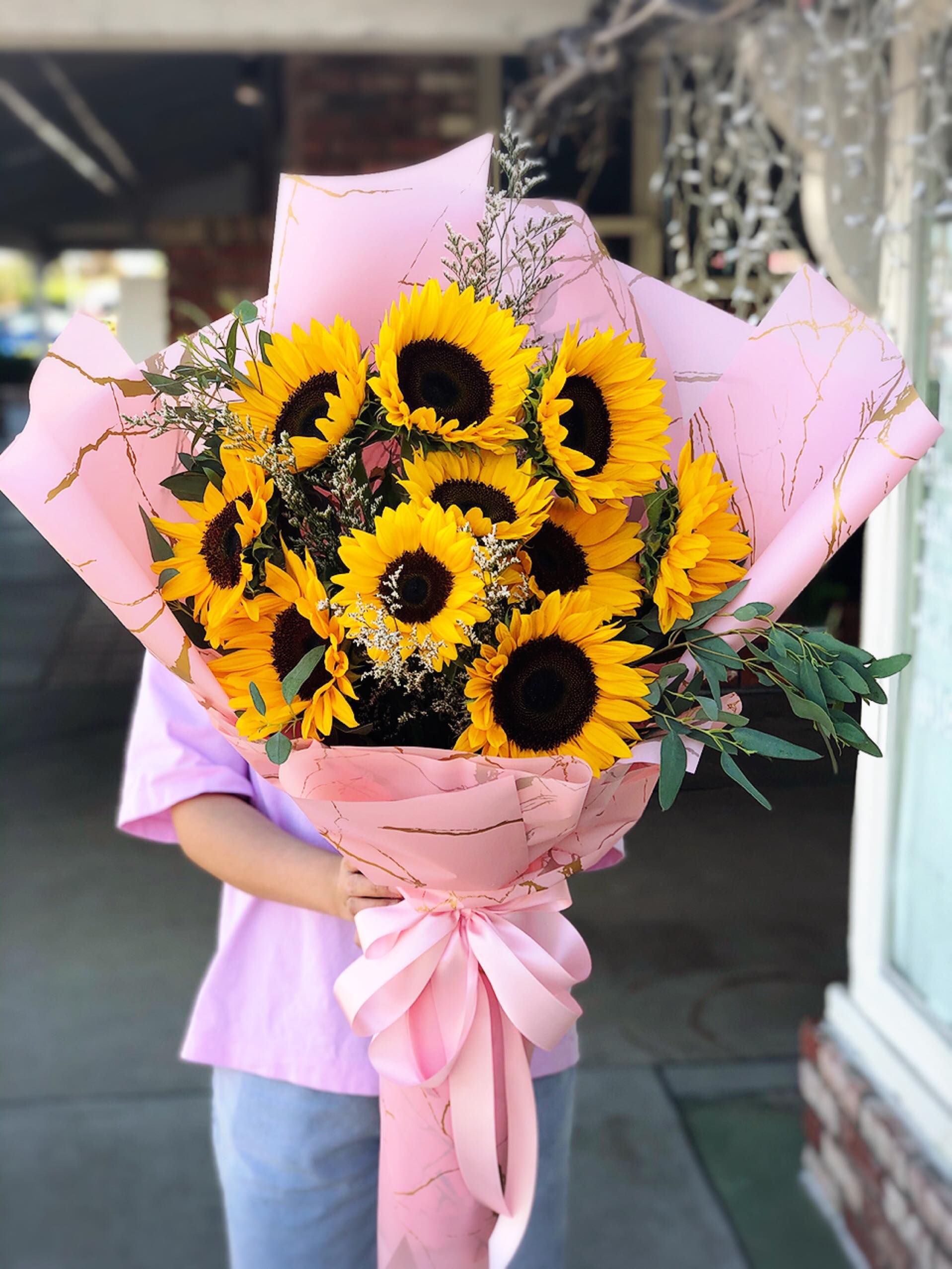 Large bouquet of sunflowers wrapped in pink paper with a ribbon