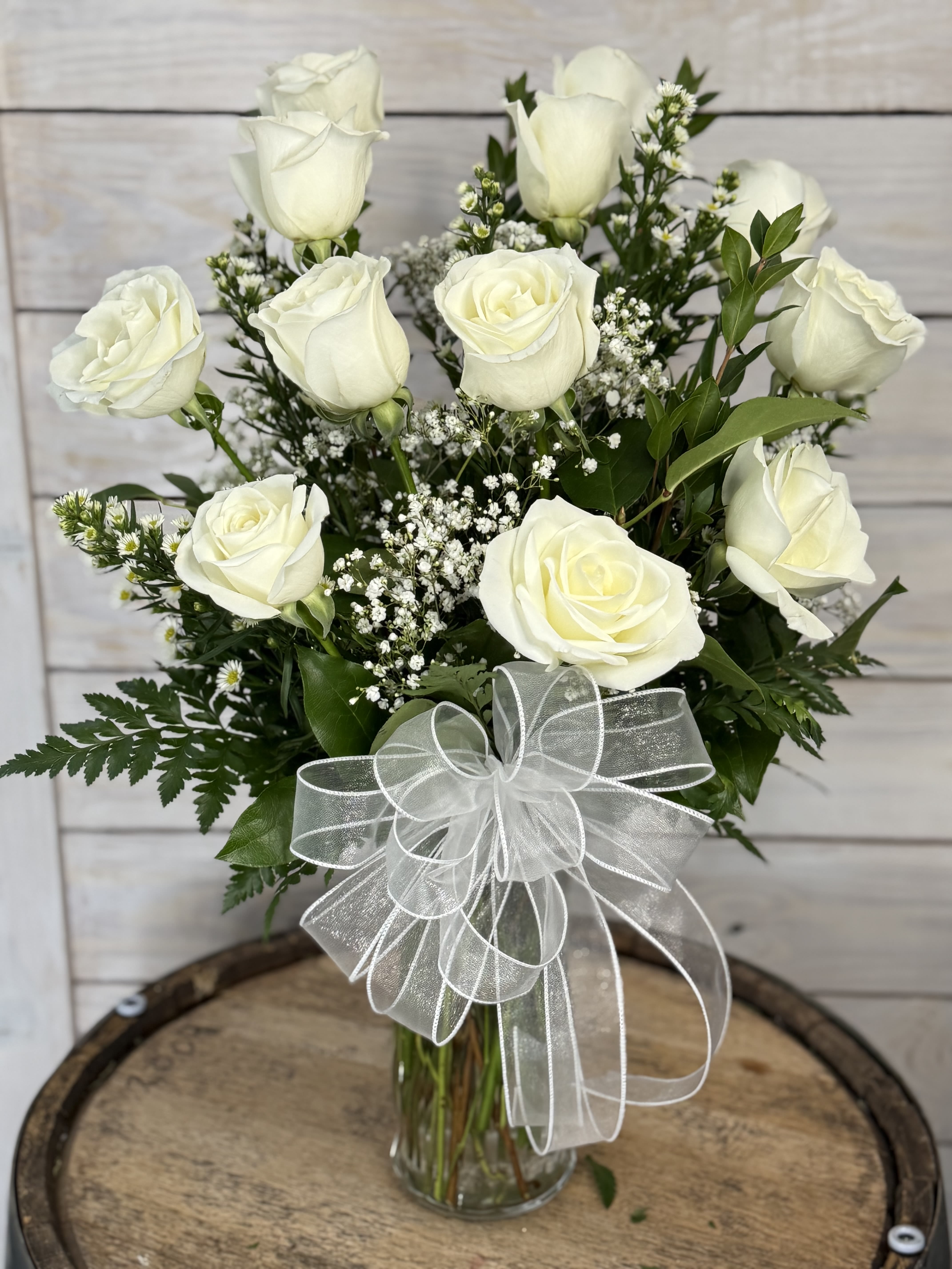 White roses in a clear glass vase with a sheer white bow
