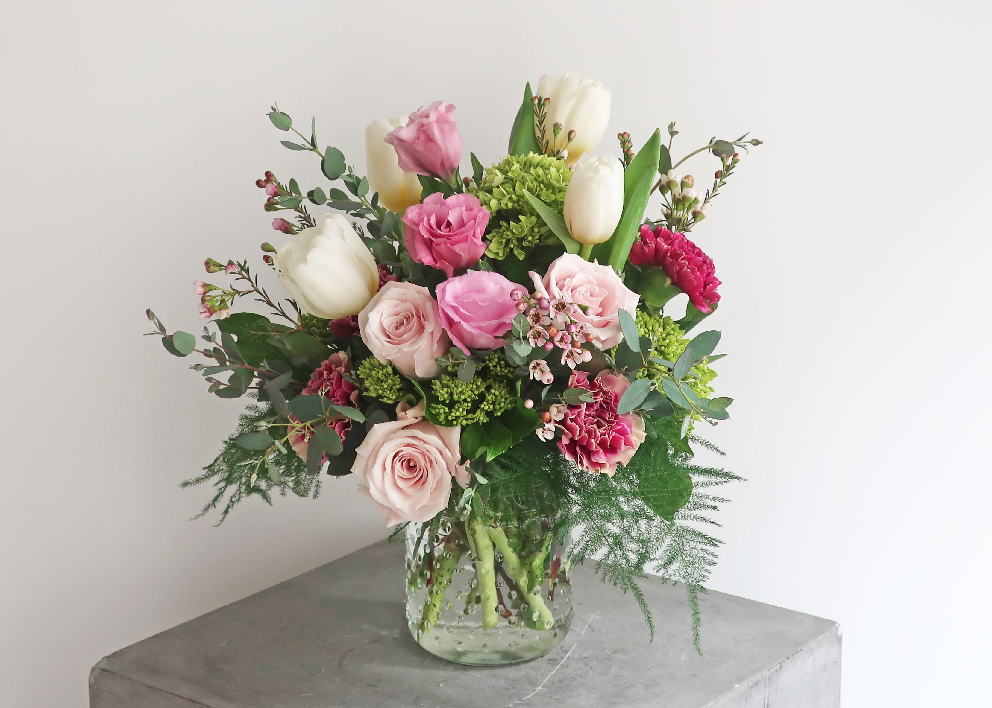 Bouquet of pink roses, white tulips, and carnations in a glass vase
