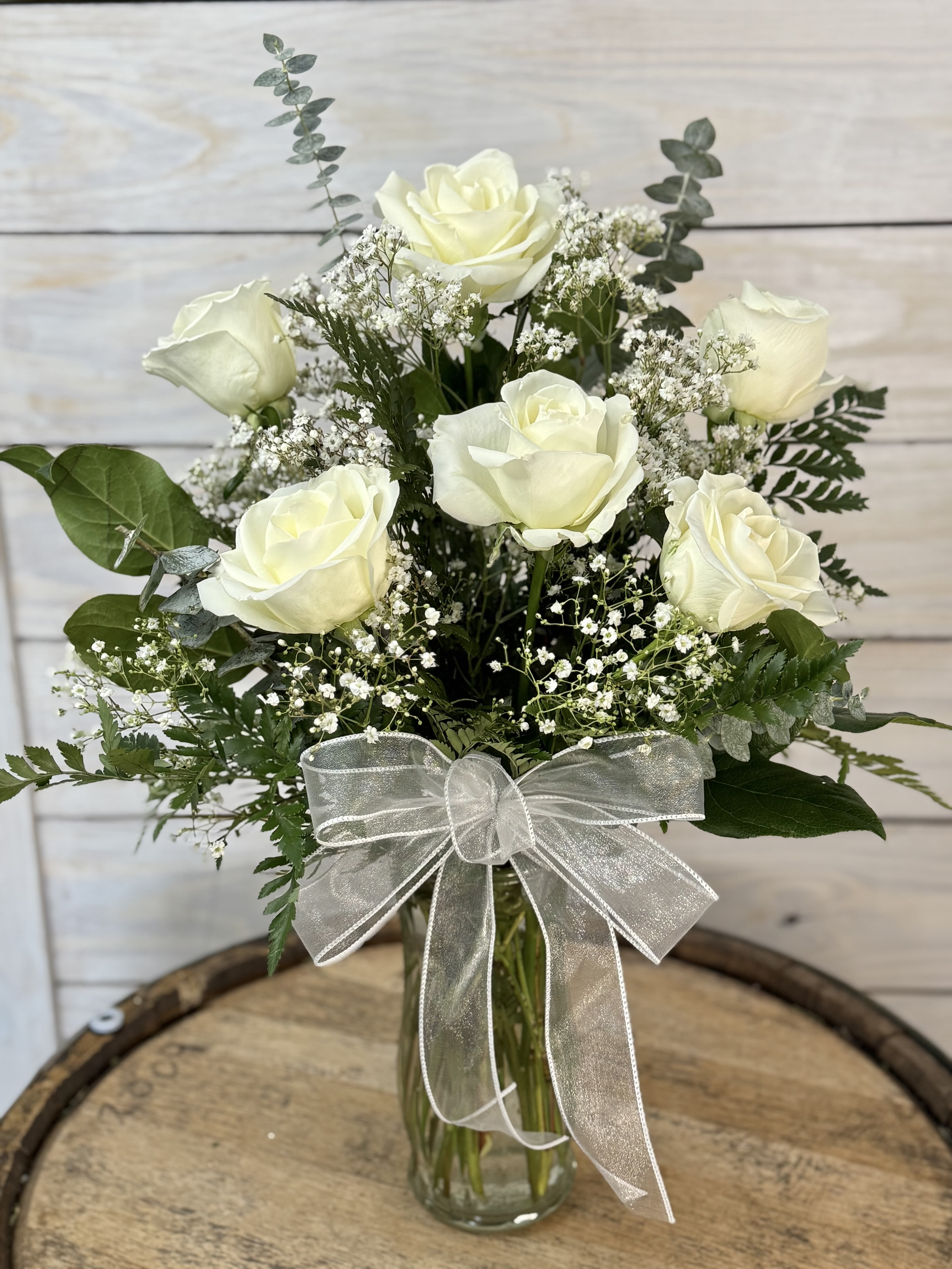 White roses in a glass vase with baby's breath and a silver ribbon