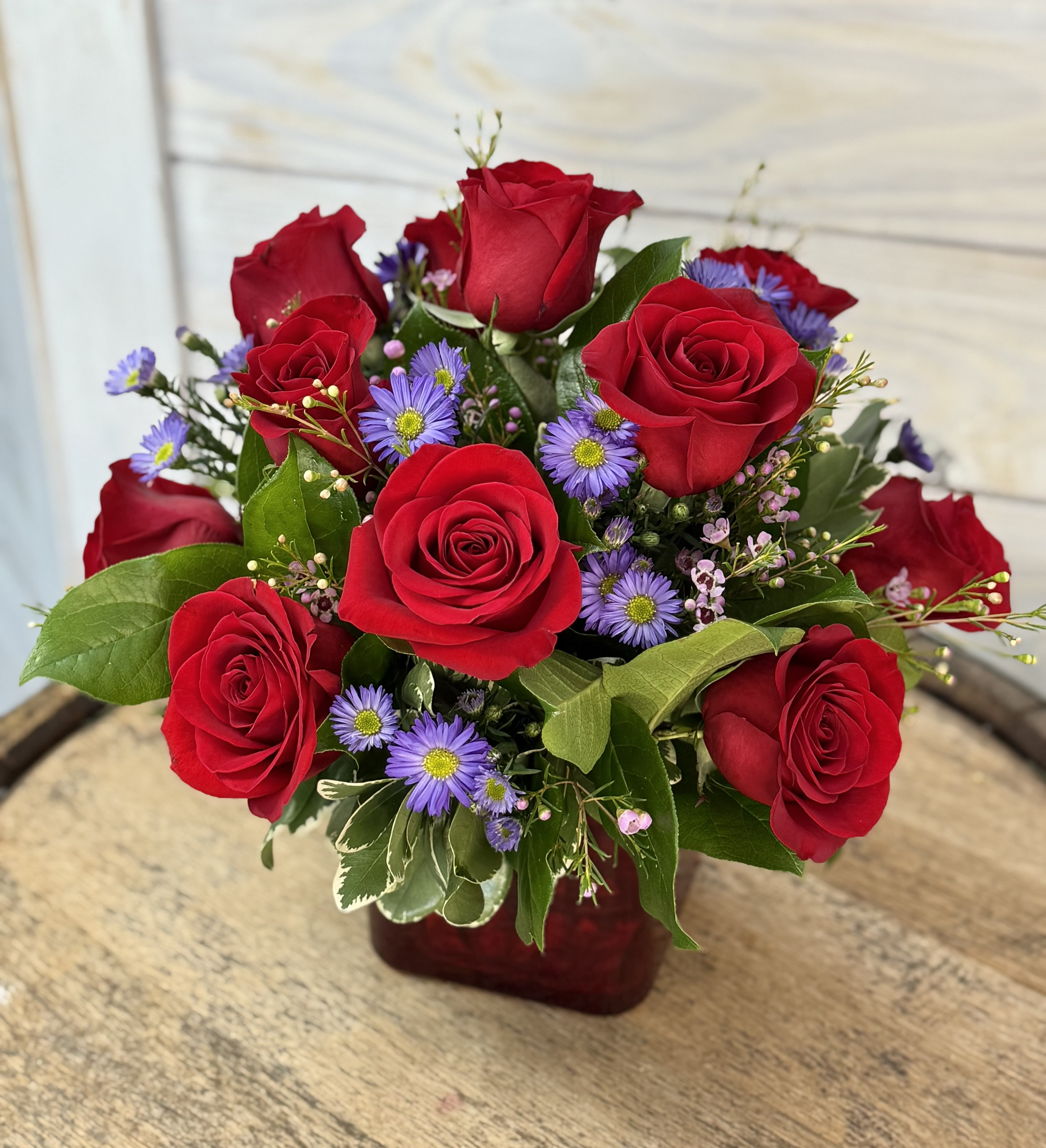 Red roses and purple daisies in a red vase