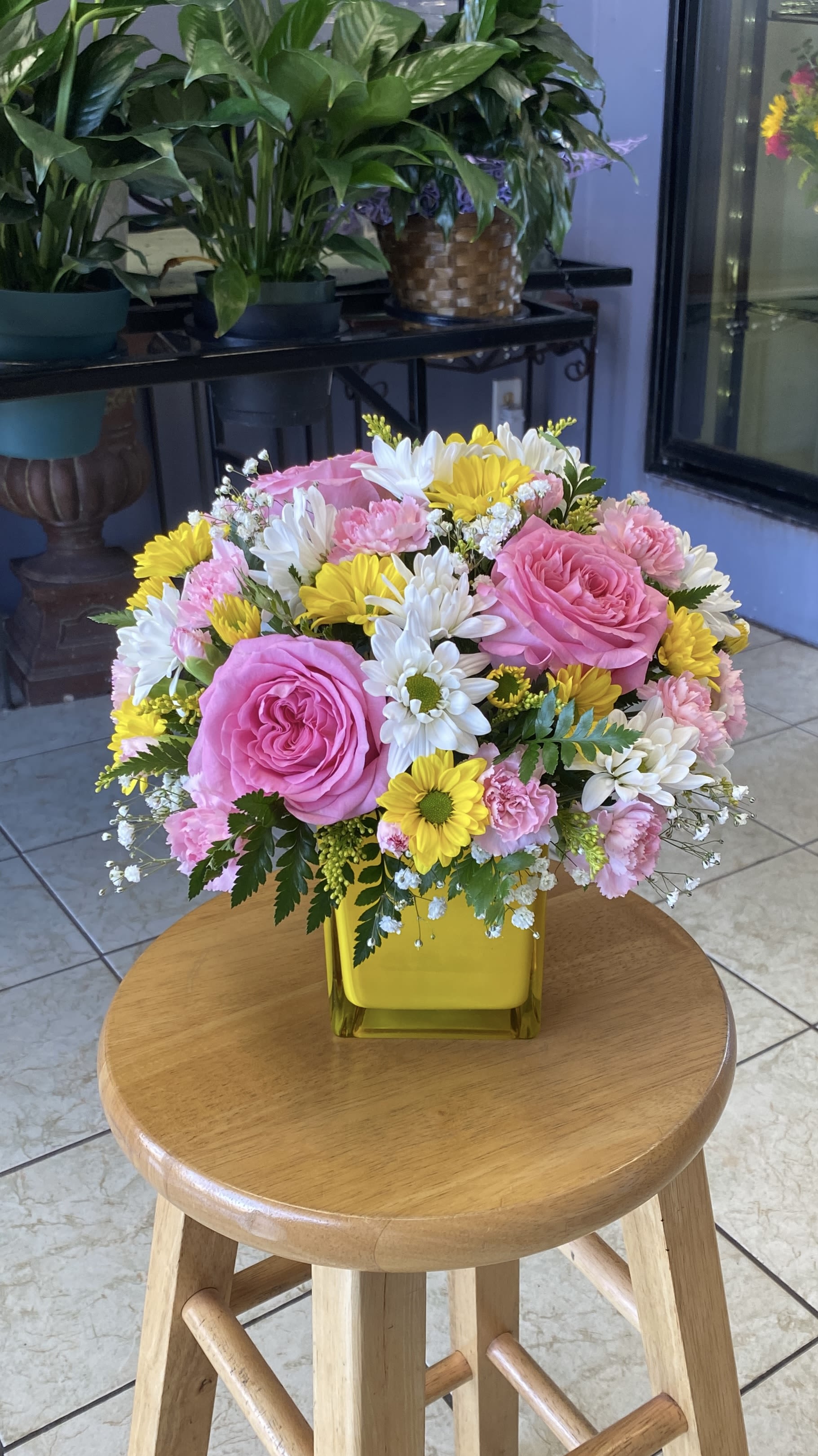Pink roses, yellow and white daisies, and carnations in a yellow vase