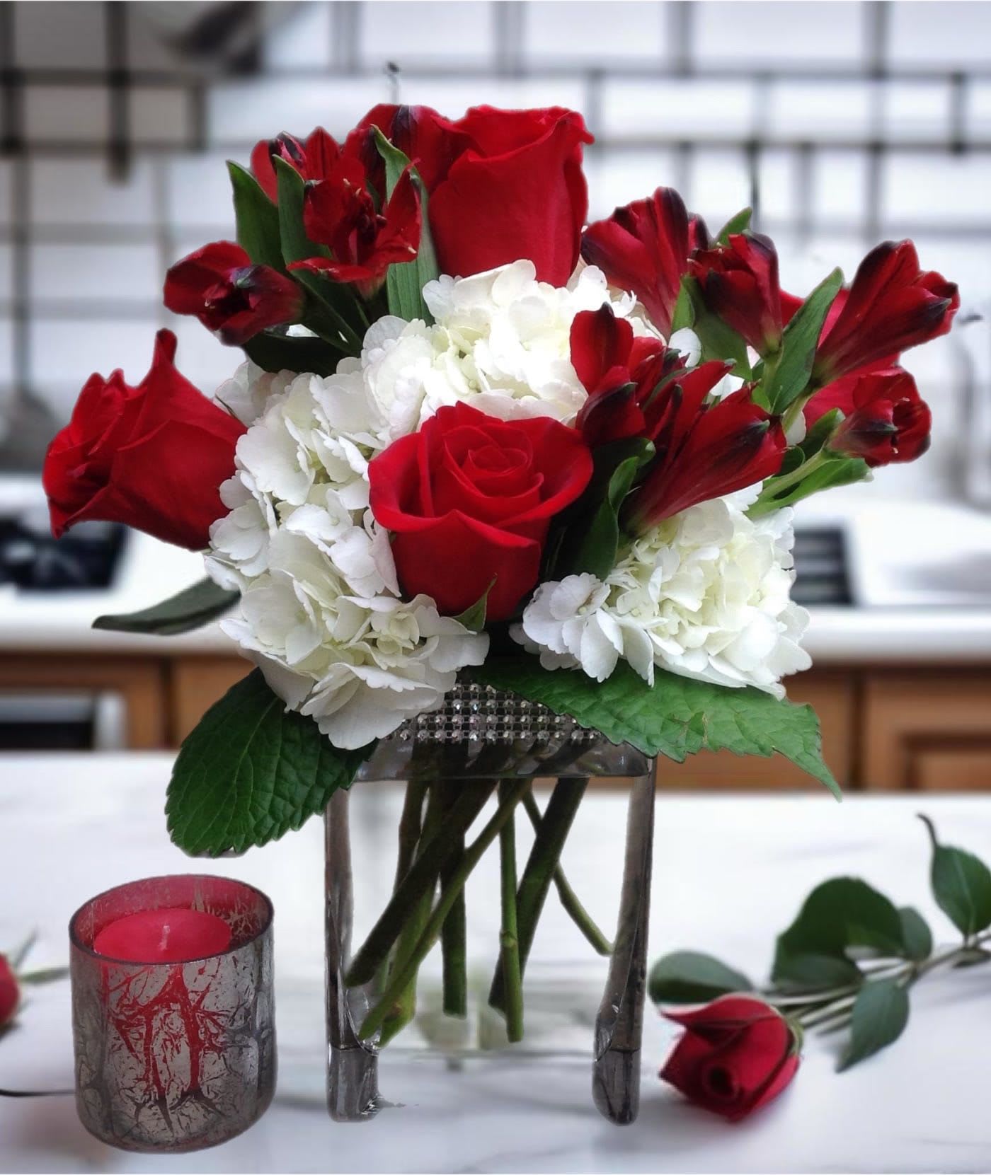 Red roses and white hydrangeas in a glass vase with a candle nearby