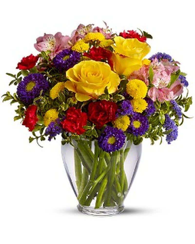 Bright mixed bouquet of yellow roses, red carnations, and purple and yellow blossoms in a clear glass vase