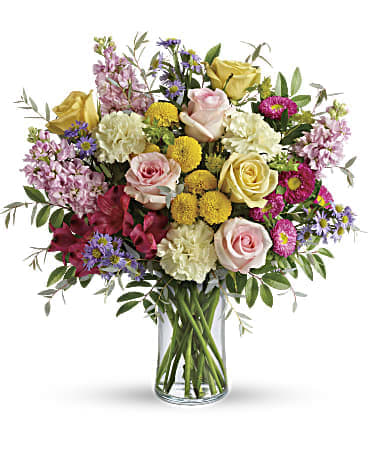 Mixed bouquet of pink and yellow roses with carnations and pompons in a clear glass vase
