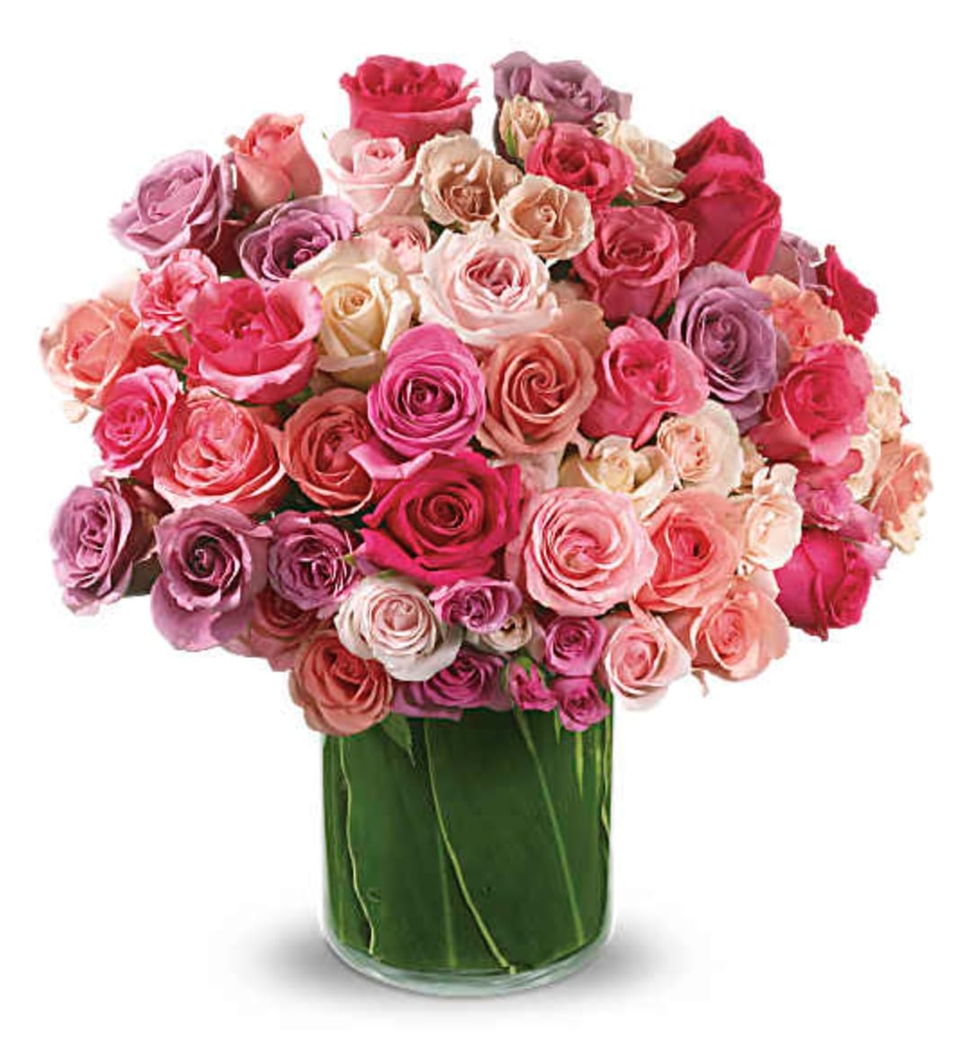 Rose Rapture Bouquet - A lush dome of roses in pink, lavender, peach and white greets the recipient with an immediate sense of joy-perfect as a birthday bouquet or a surprise for an anniversary, Mother's Day, or just because. The Rose Rapture arrangement reads romantic and celebratory at once: vivid hot-pink and deep-magenta blooms pop against softer blush, peach and lavender roses to create a feminine, garden-fresh impression that makes the person you're thinking of feel truly cherished.  Tightly packed into a clear cylindrical glass vase, the roses form a full, rounded silhouette with a polished, modern finish; long greenery layered in the vase adds a clean vertical line and natural contrast. The design is substantial without feeling fussy-ideal for love and romance, a meaningful thinking-of-you gesture, or to mark a milestone birthday. Available in a generous size that fills a table or bedside, these roses arrive ready to display; refresh vase water every two days and trim stems if needed to keep blooms at their best.