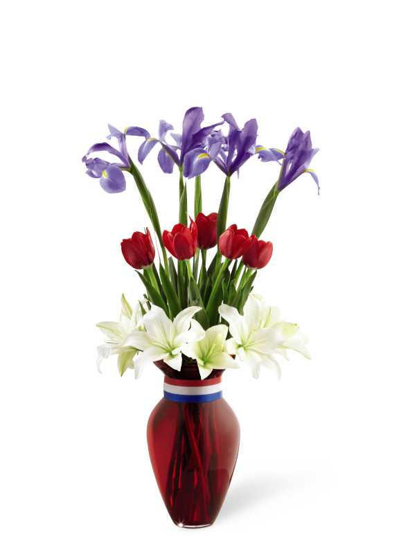 The FTD Greater Glory Bouquet - The FTD Greater Glory Bouquet is an inspiring way to honor the life of a soldier at their final memorial. White Asiatic lilies, red tulips and blue iris are arranged in a tiered fashion and seated in a red glass vase accented with a red, white and blue ribbon around the neck to create an exceptional presentation of patriotic beauty.