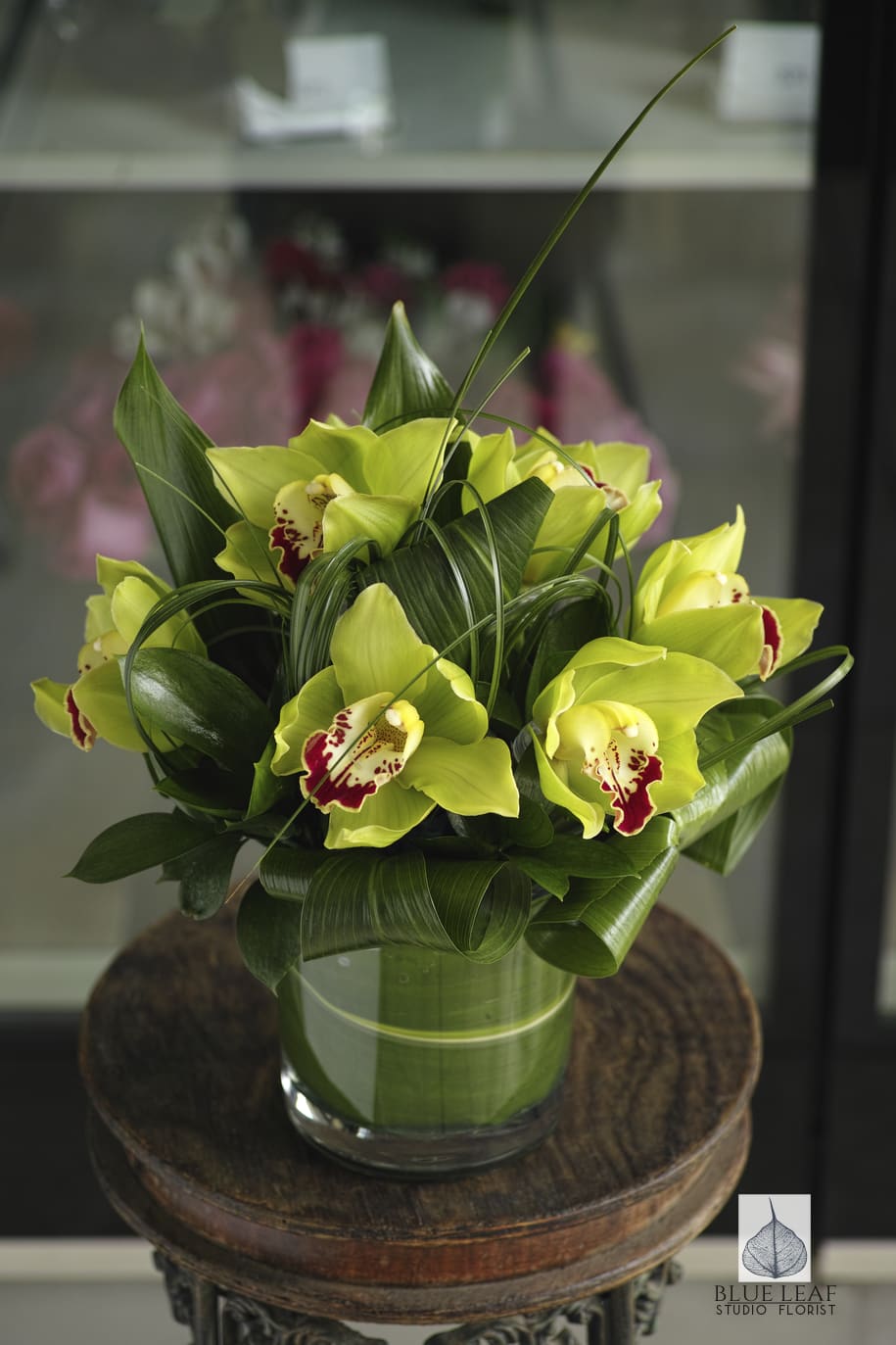 Green Orchid Obsession - A short, modern bouquet of green cymbidium orchids with ti leaves and loops of bear grass to create a fabulous centerpiece for all occasions. 
