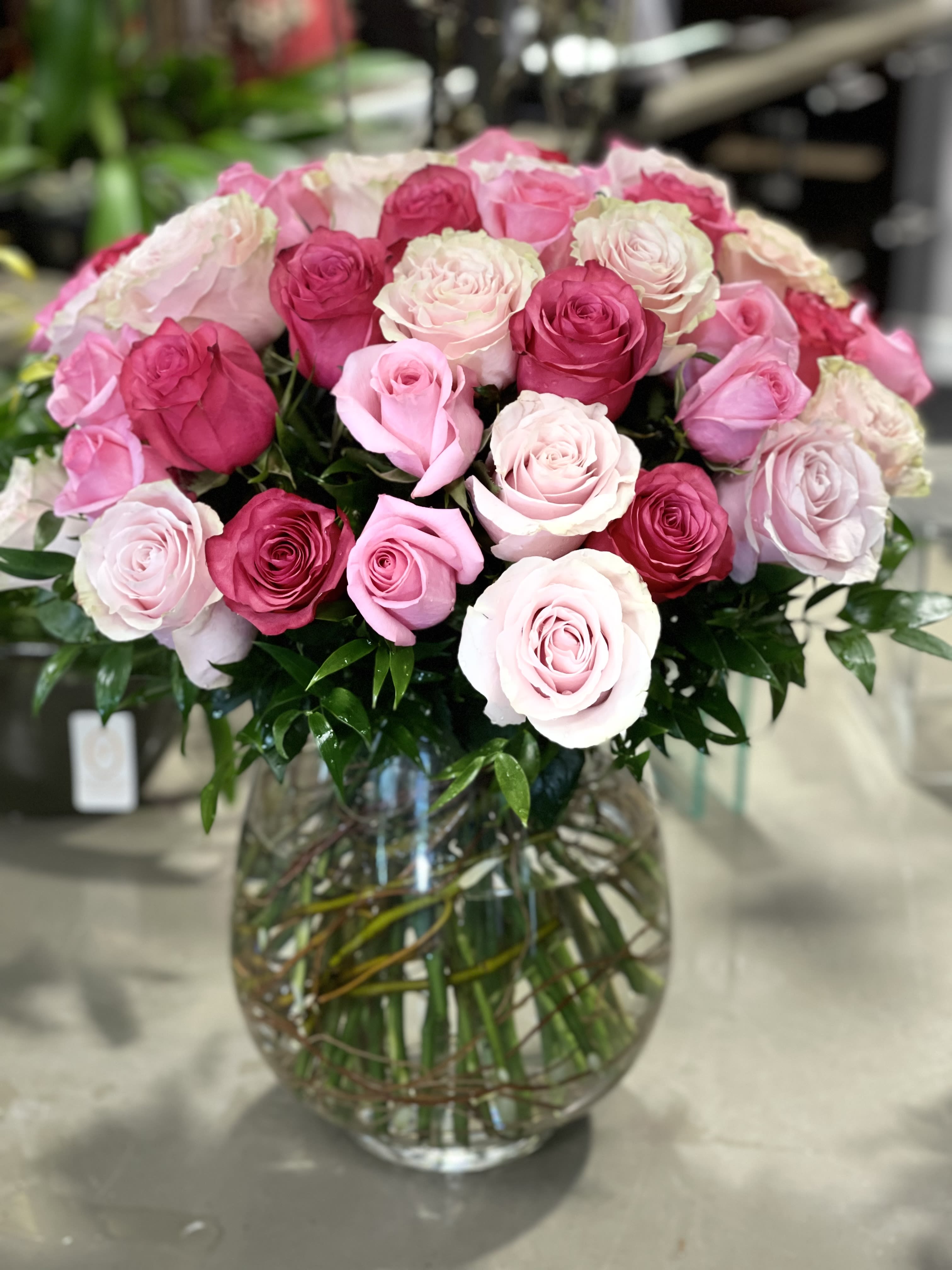 Large bouquet of pink roses in varying shades arranged in a round clear glass vase.