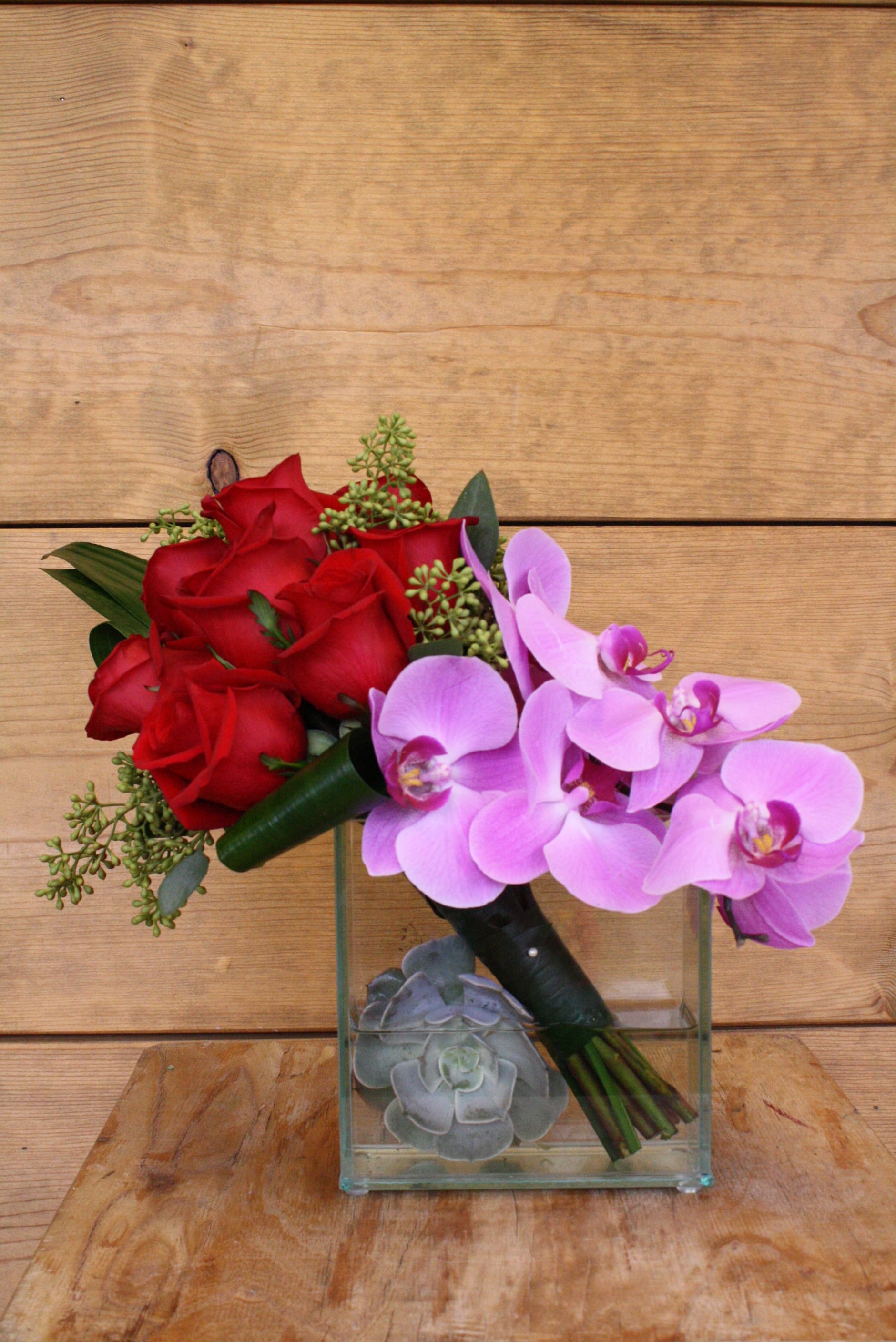 Red roses and pink orchids in a glass cube vase with succulents