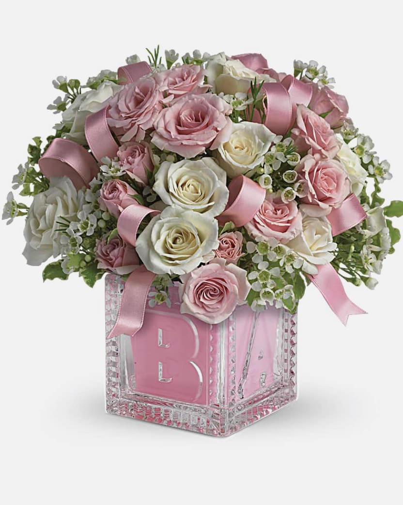 Pink and white roses arranged in a glass block vase with ribbon